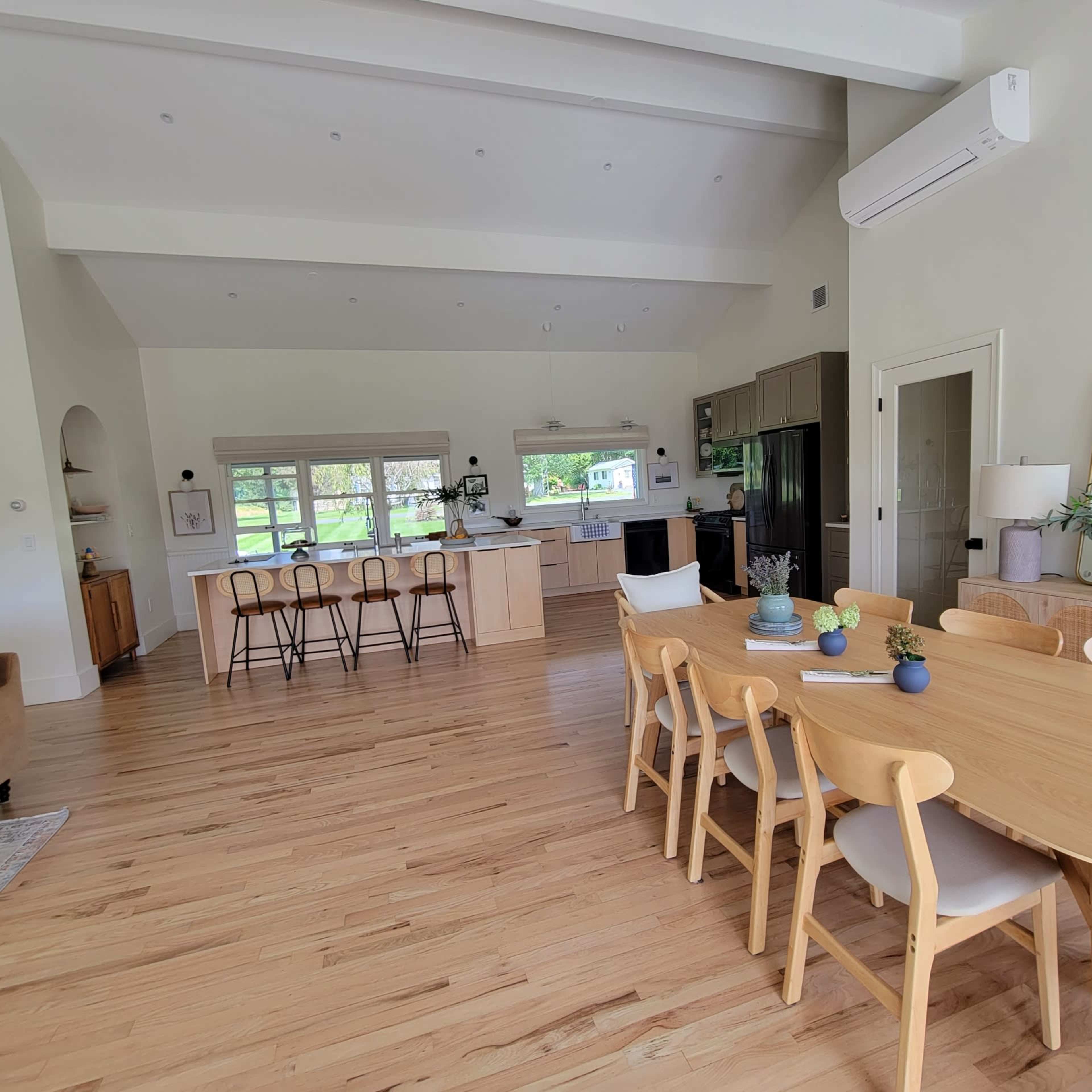 A spacious, open-concept living area featuring a dining table, kitchen island, and seating area with large windows letting in natural light.