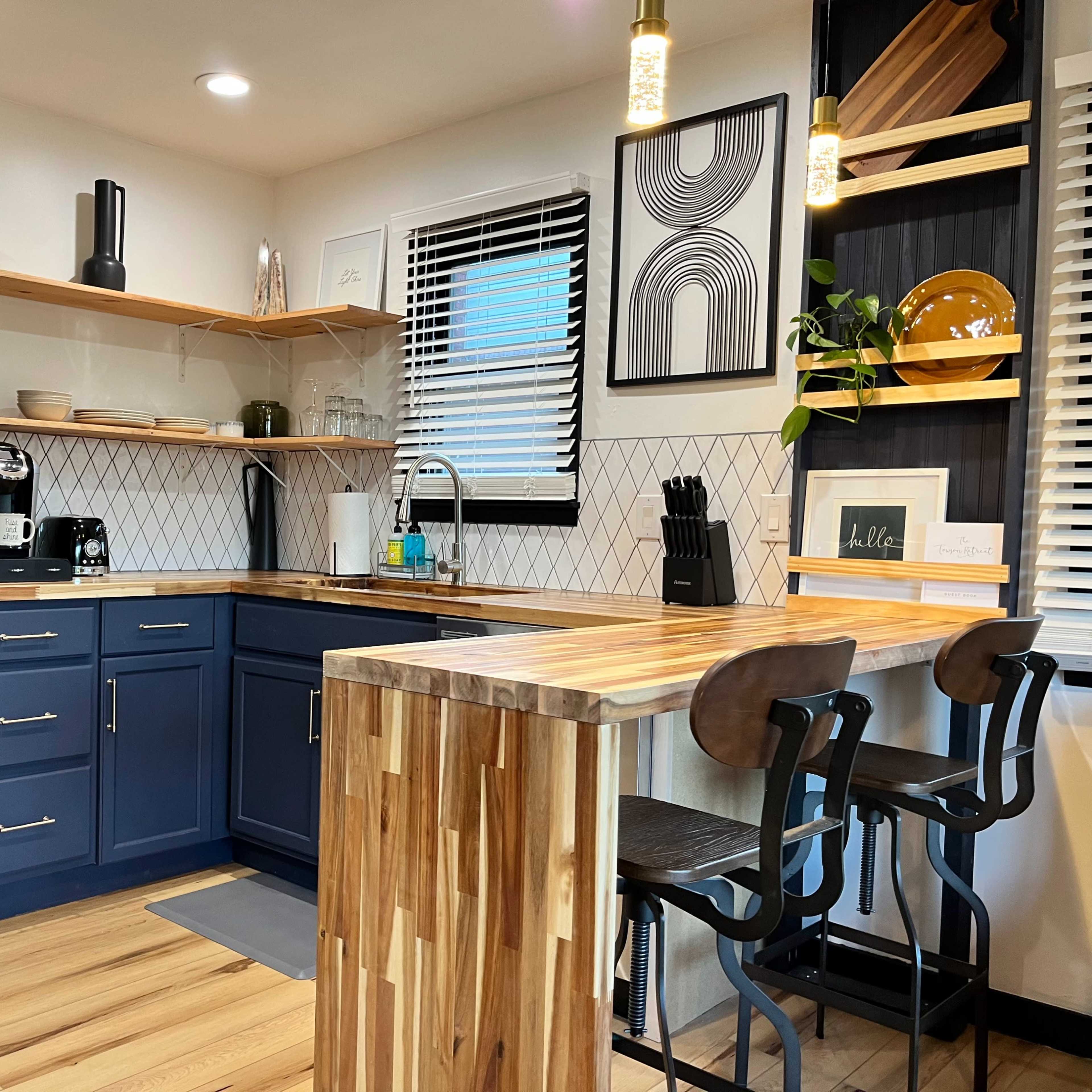 A modern kitchen with navy blue cabinets, wooden countertops, a coffee maker, and bar seating with two stools.