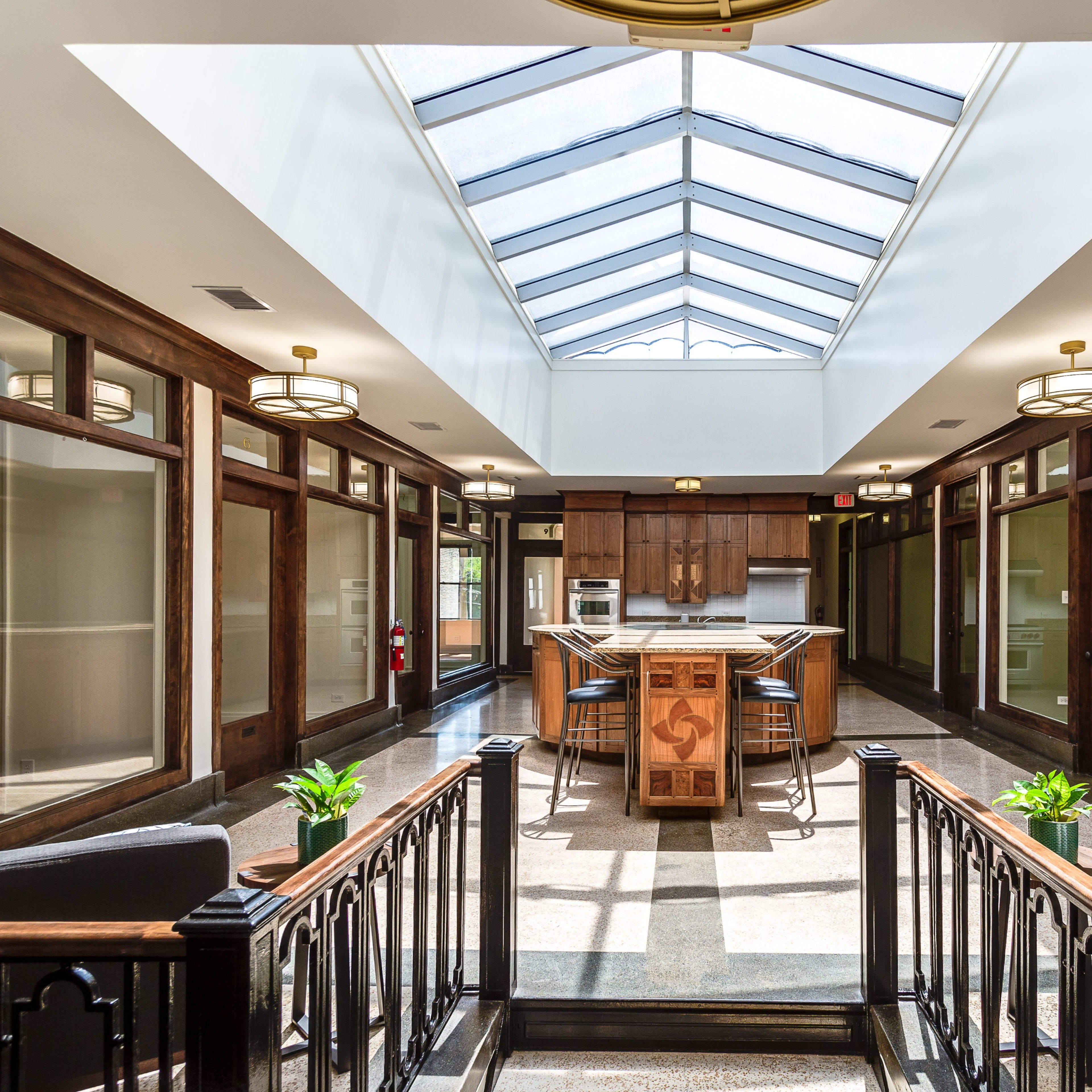 A bright, open kitchen area with a skylight, surrounded by wooden paneling and seating areas, leading to rooms on either side.