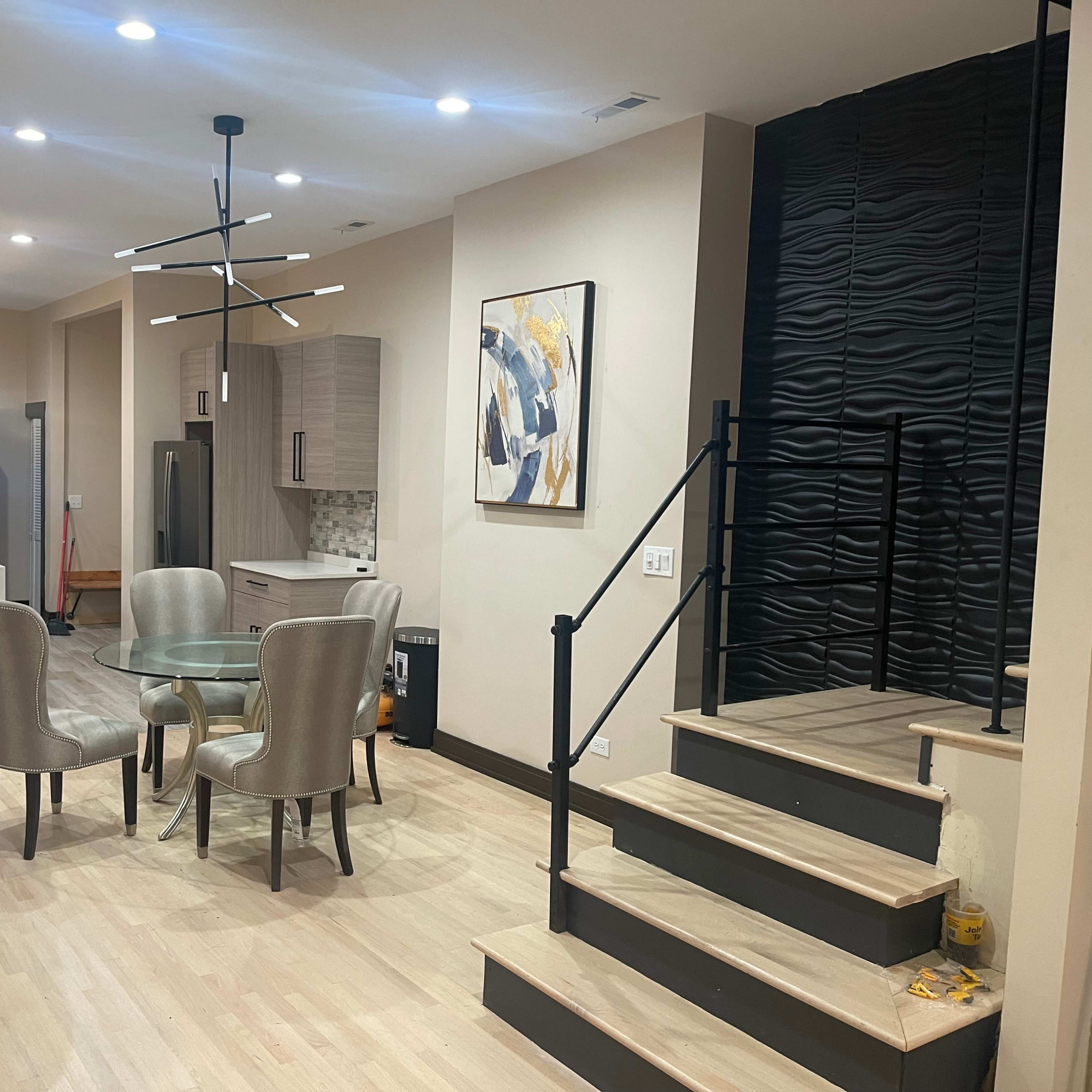 A modern interior features a dining area with a glass table and four chairs, leading to a kitchen with sleek cabinetry and an adjacent staircase.