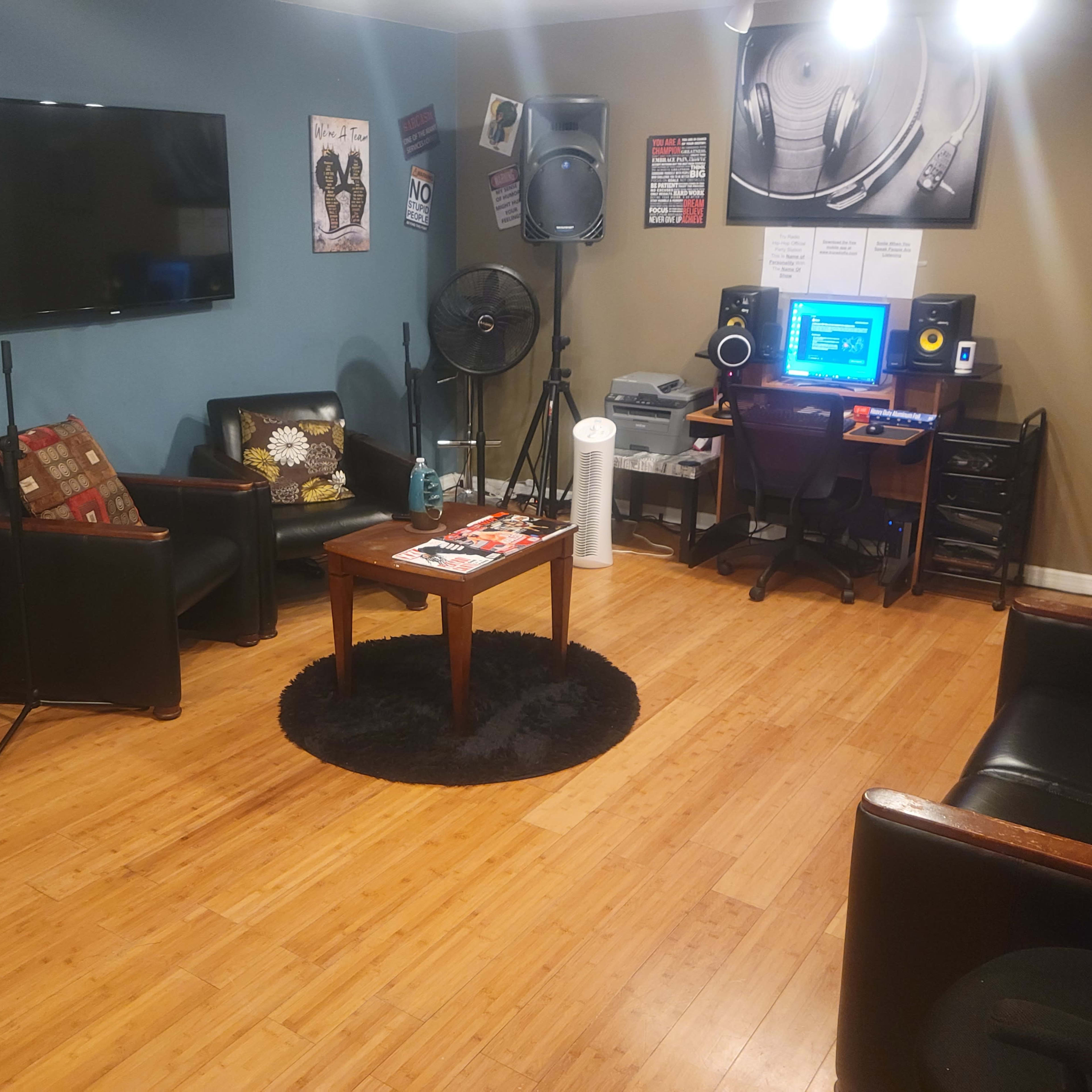 The room features two black leather sofas, a wooden table, a television, a computer setup for music production, and various audio equipment.
