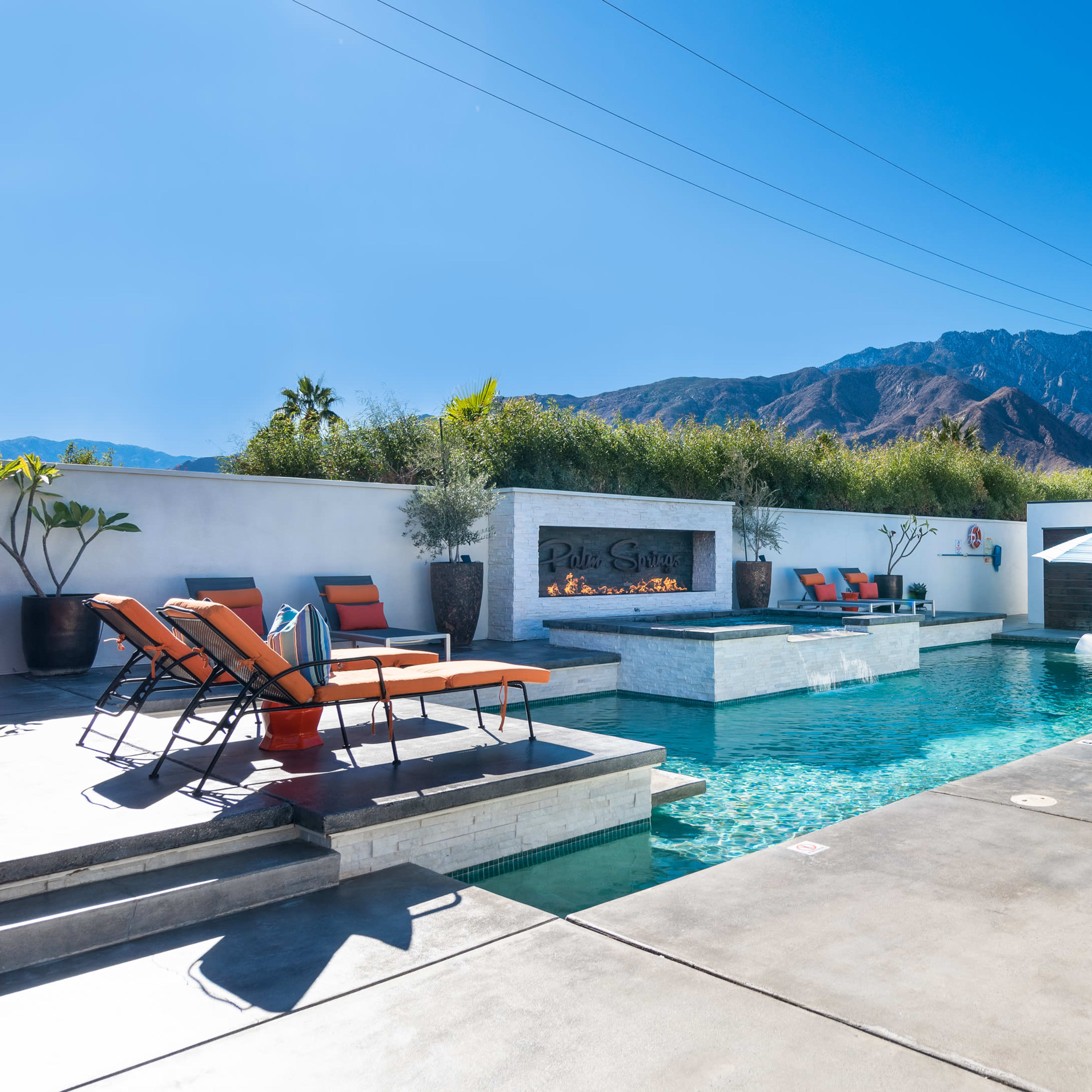 A modern backyard with a rectangular pool, lounge chairs, and a mountain backdrop.