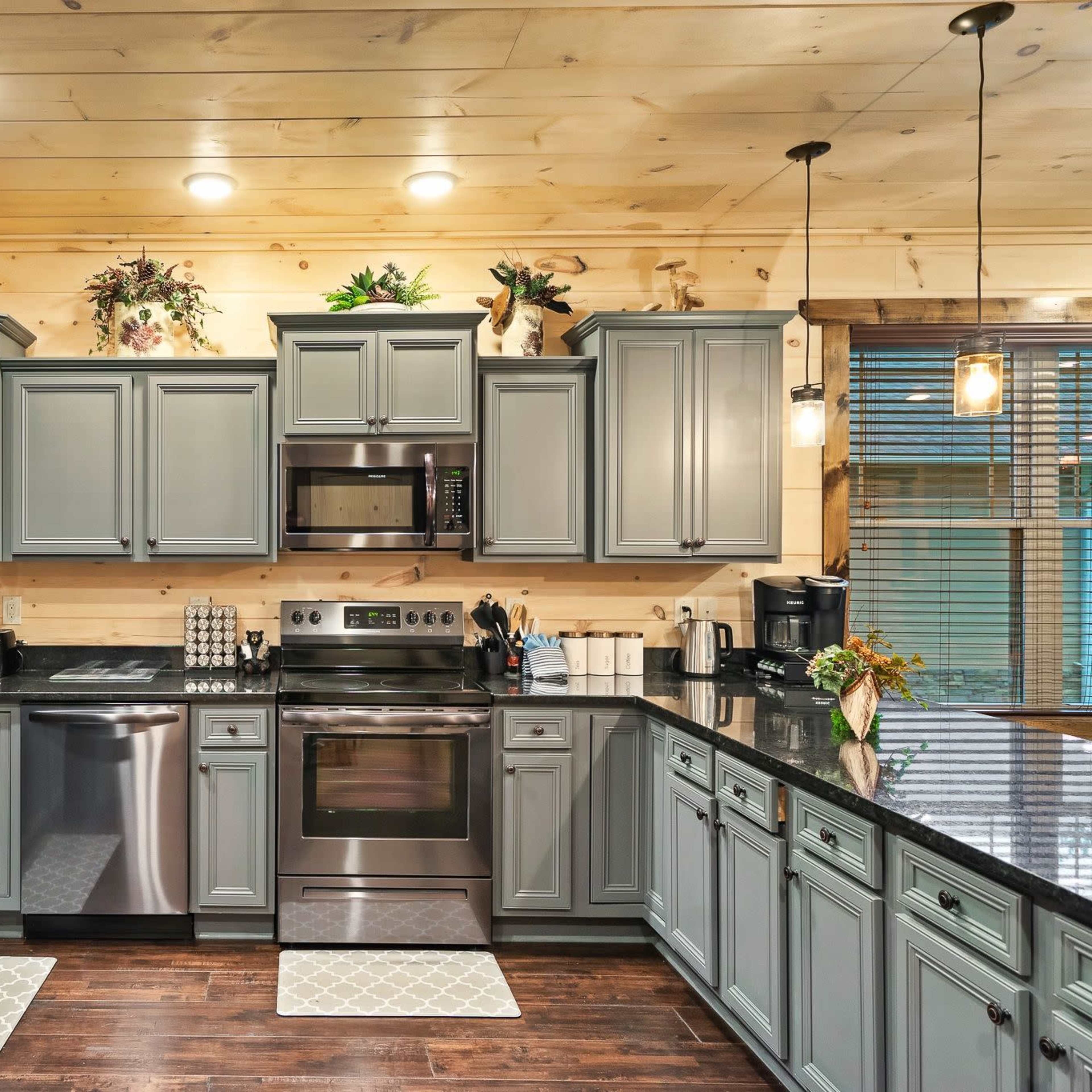 A modern kitchen features gray cabinets, stainless steel appliances, and a combination of dark countertops and light wooden walls.