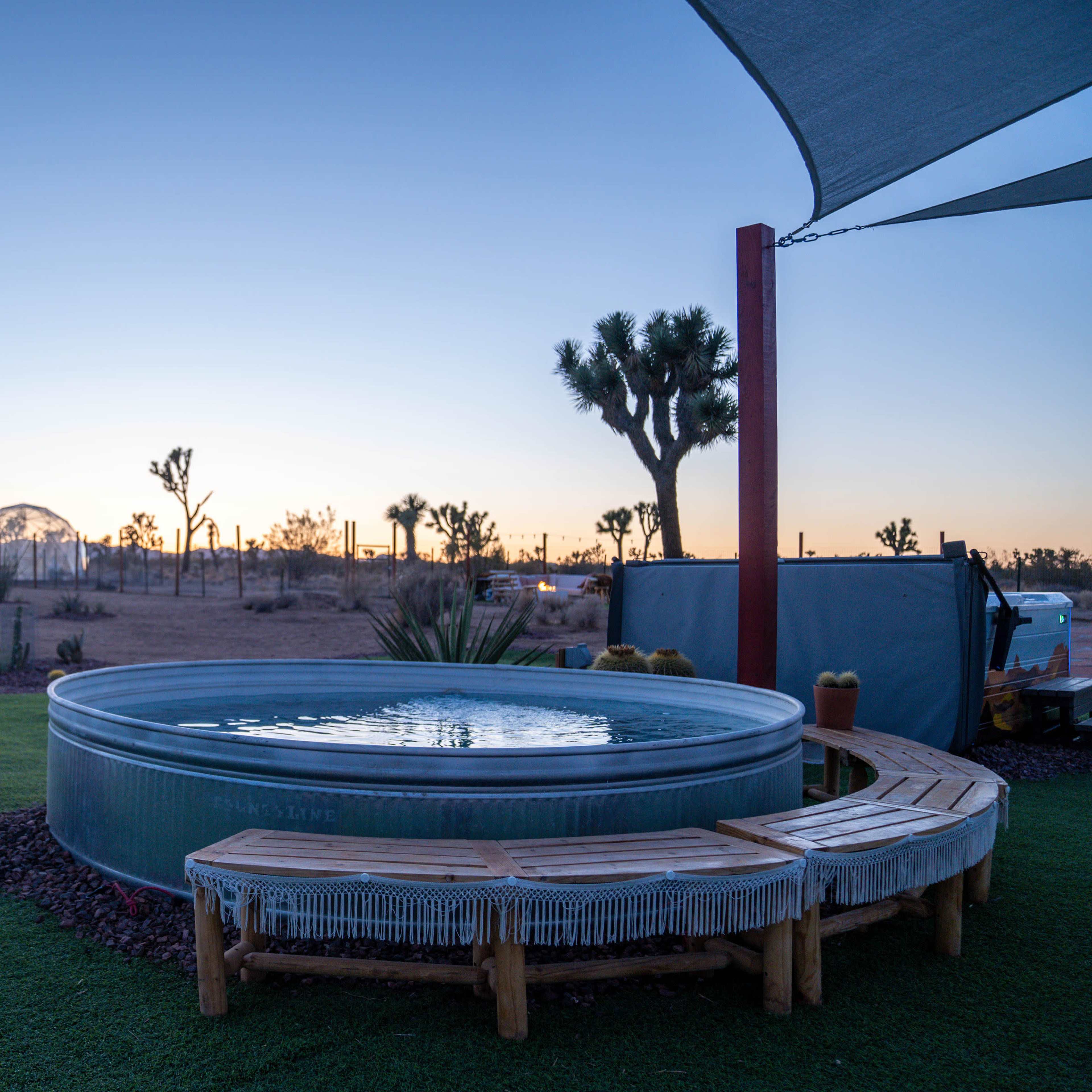 A hot tub is positioned on a grassy area, surrounded by desert landscaping and with a clear sky at dusk in the background.