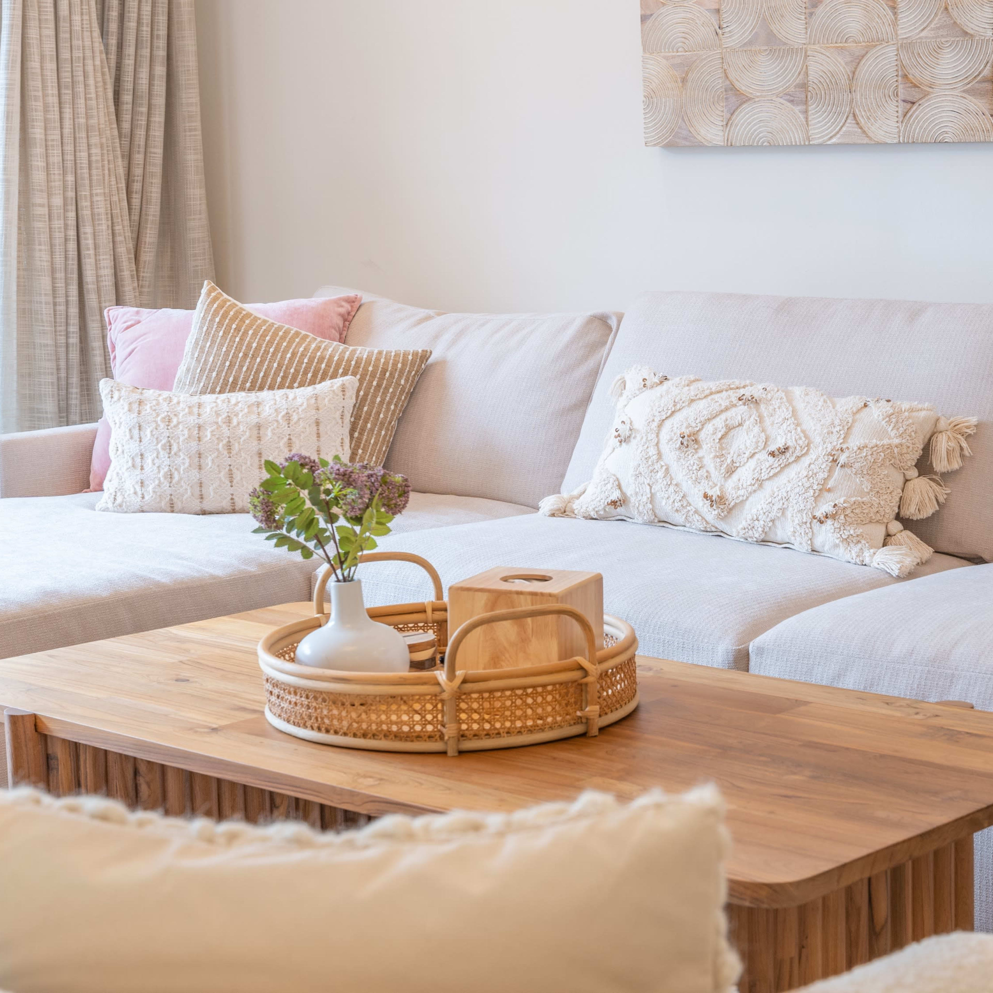 A light-colored sectional sofa is arranged with decorative pillows beside a wooden coffee table displaying a small plant and a vase of flowers.