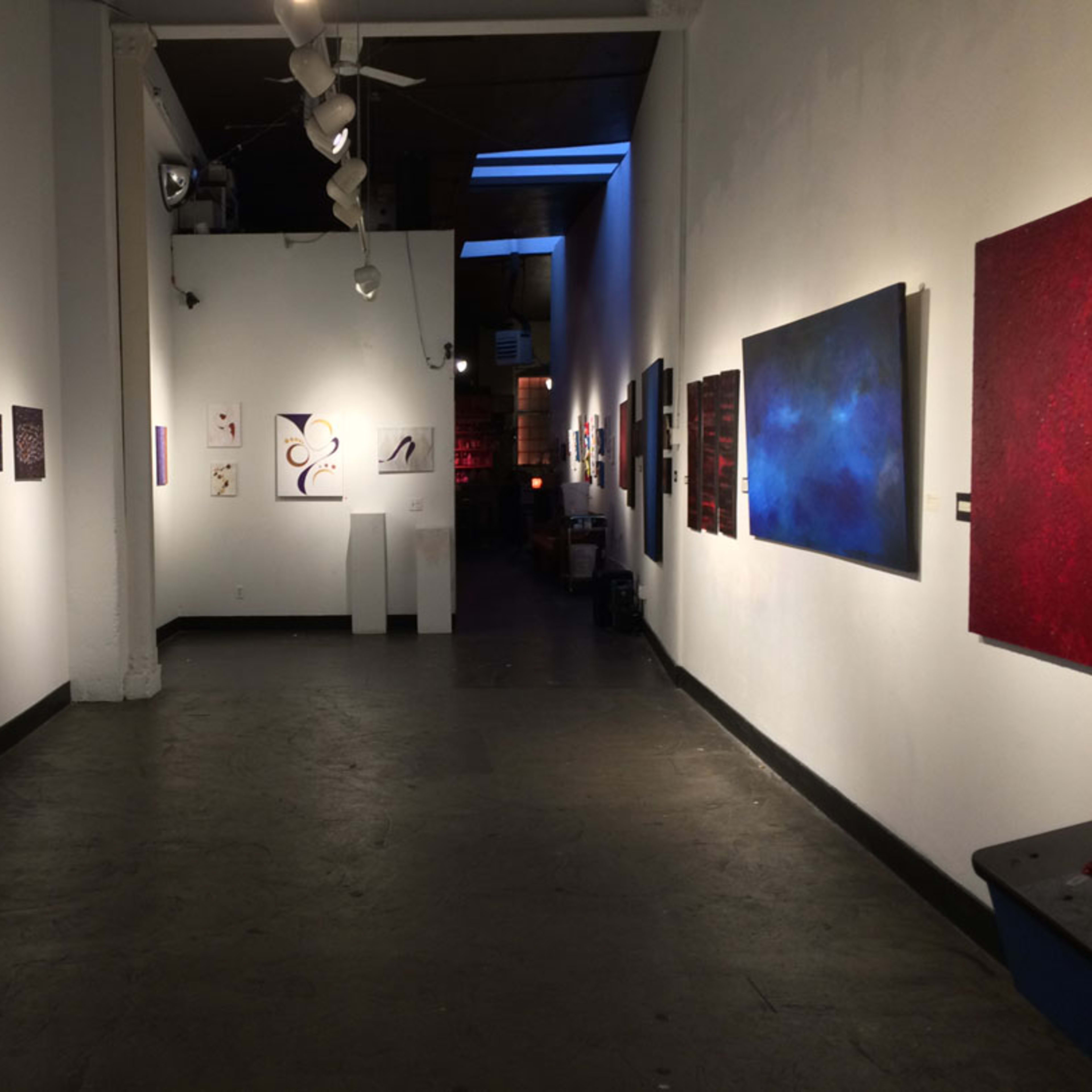 An art gallery with various framed artworks displayed on the walls and a dark floor.