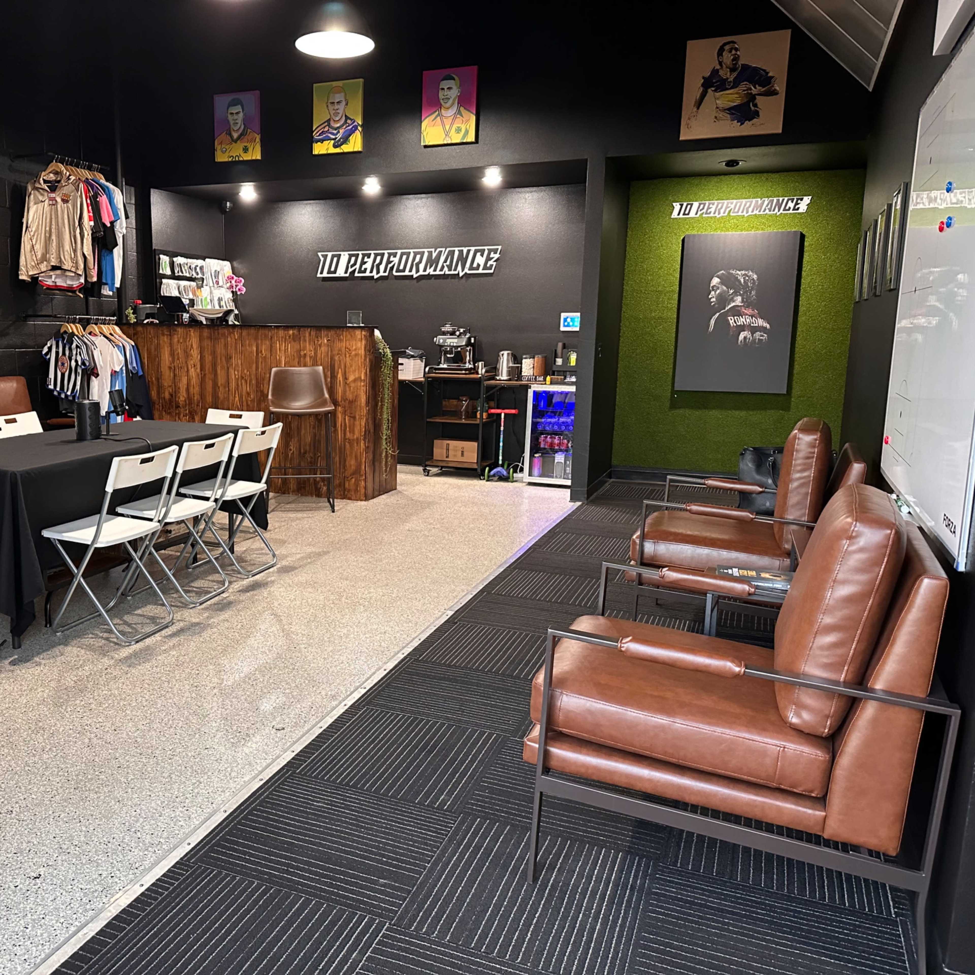 An indoor space designed for meetings and training, featuring a table with chairs, a lounge area with leather seating, and a display of sports apparel on the wall.