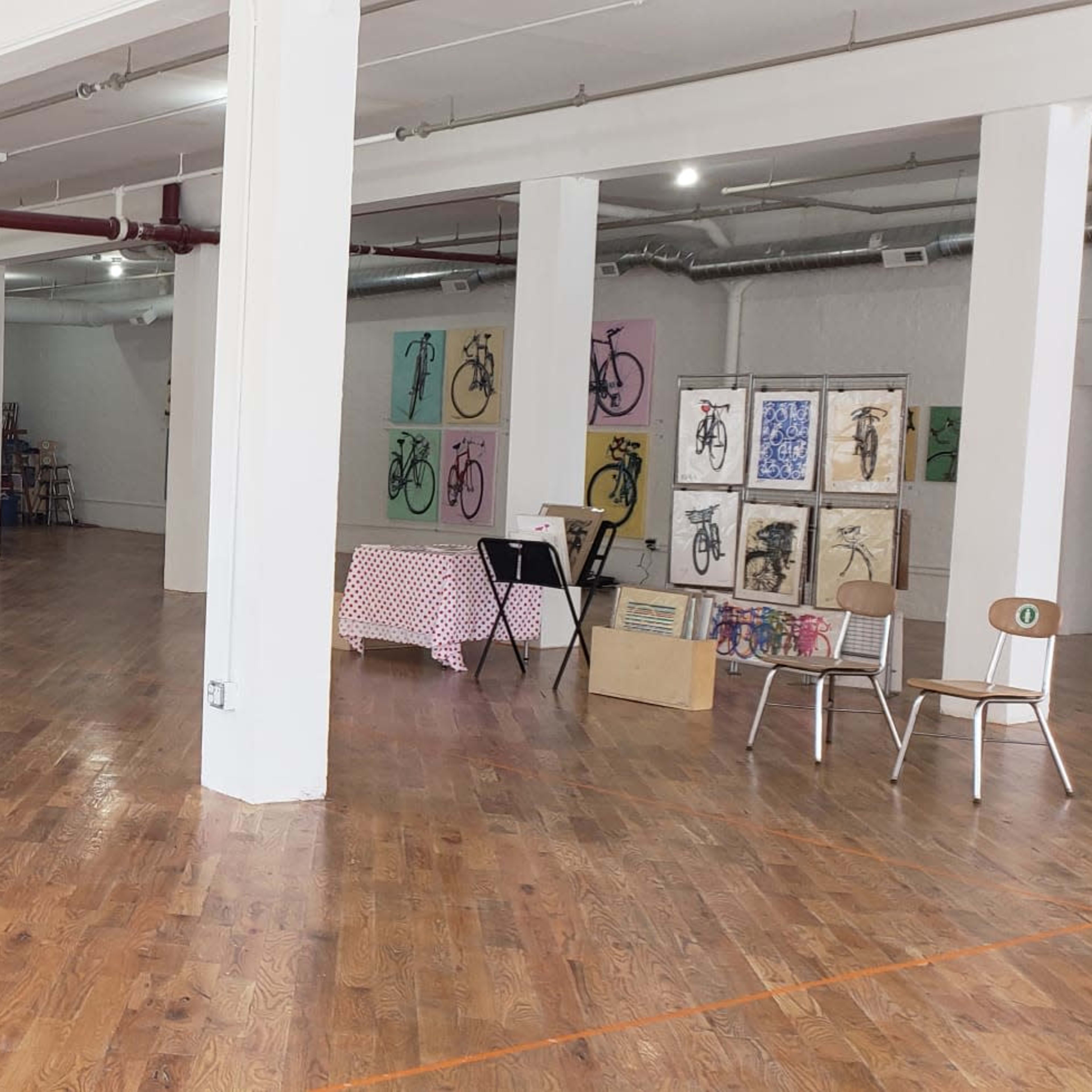 A spacious, empty art studio with polished wooden floors, white walls, and various artworks displayed around the room.