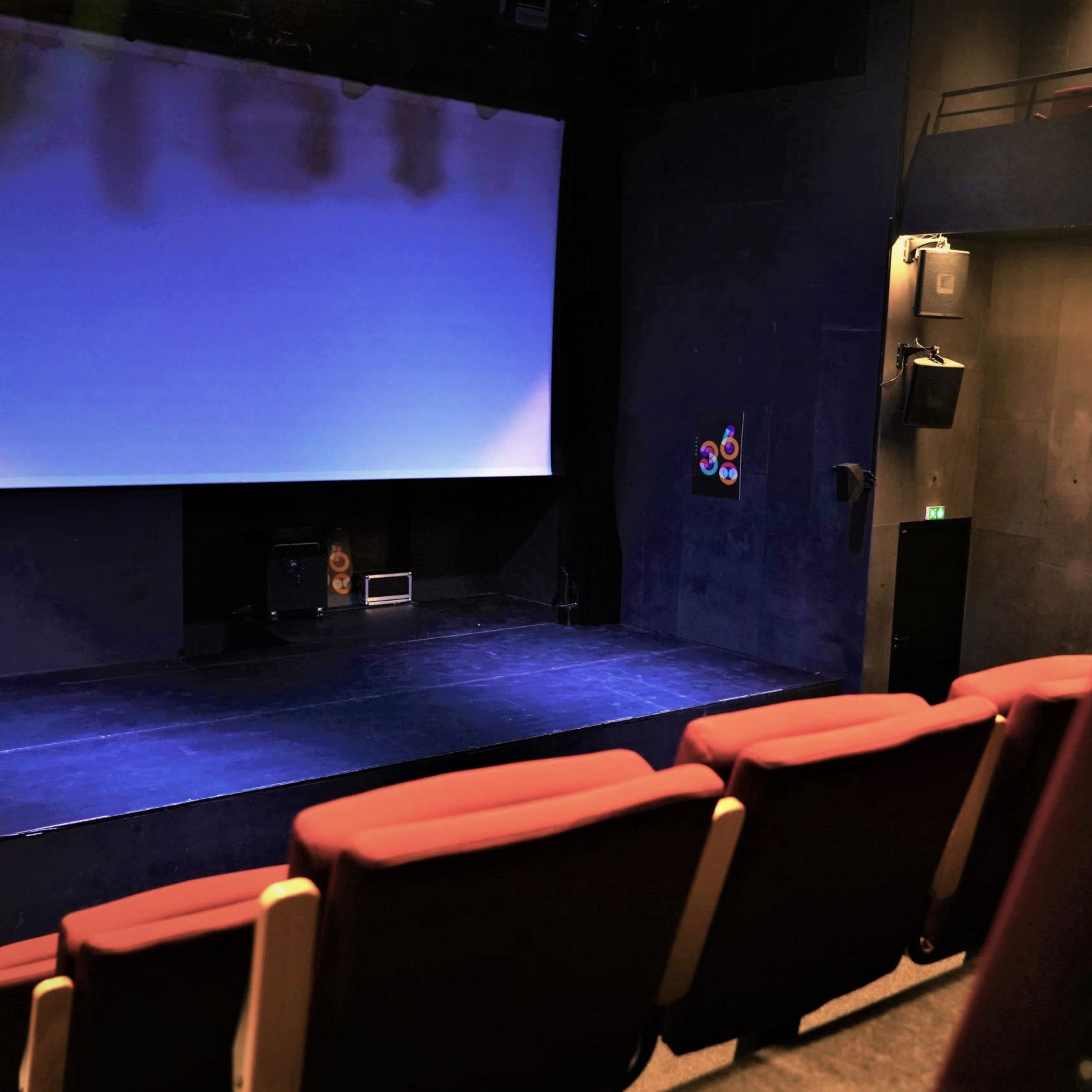 An empty theater with red seats facing a dark stage and a blank screen.