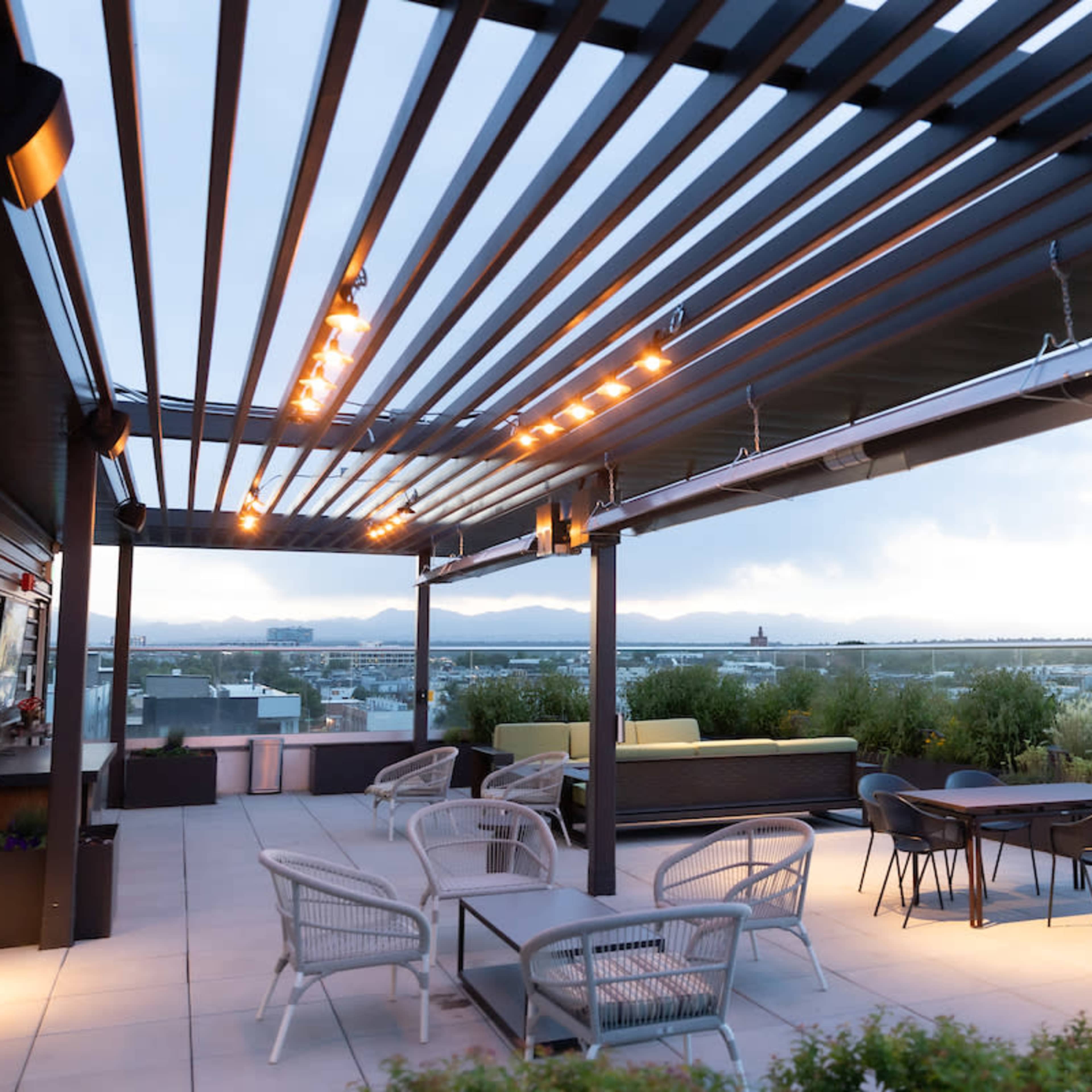 A rooftop terrace featuring modern furniture, overhead lighting, and a view of the surrounding landscape.