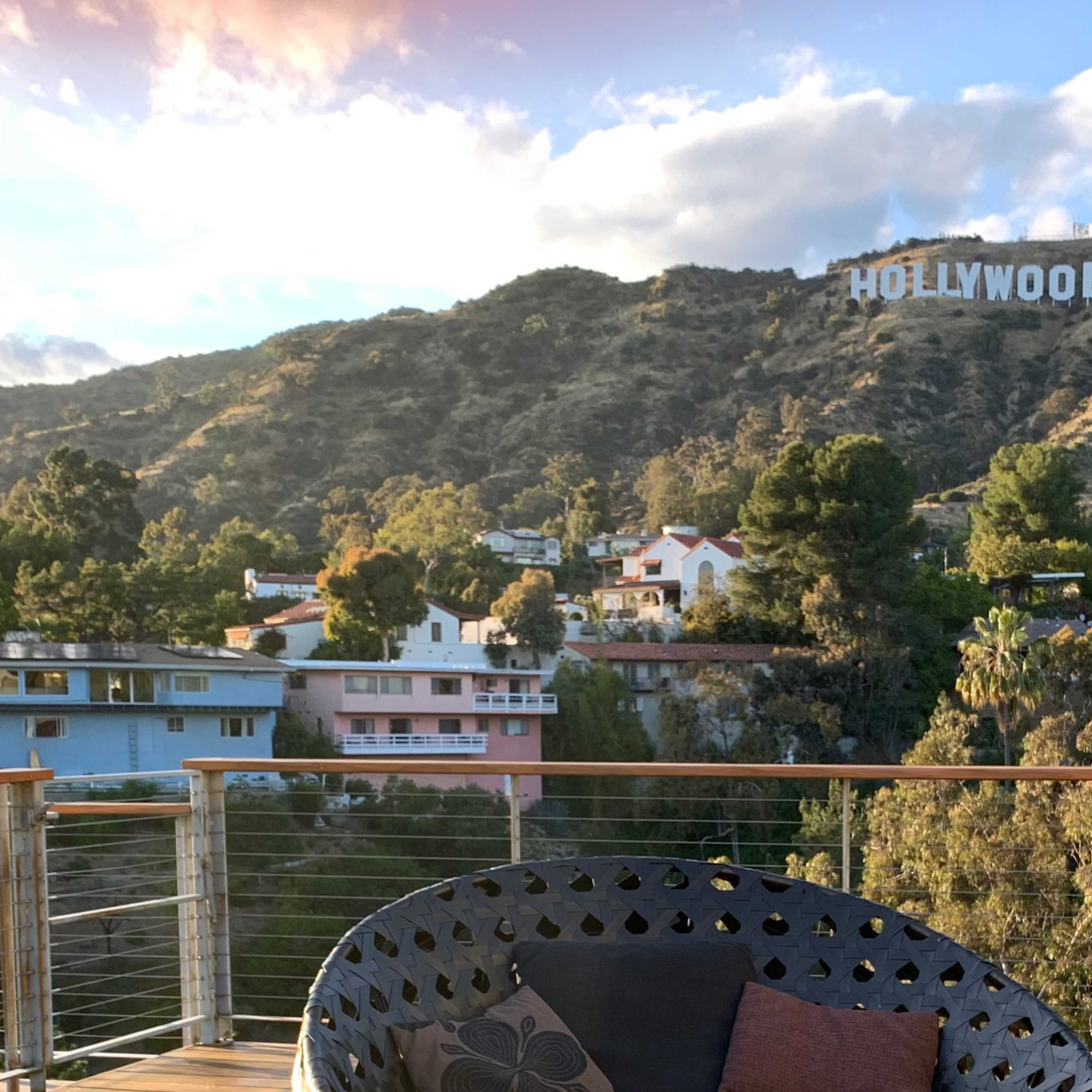 The Hollywood sign is visible on a hillside above houses nestled in a valley.