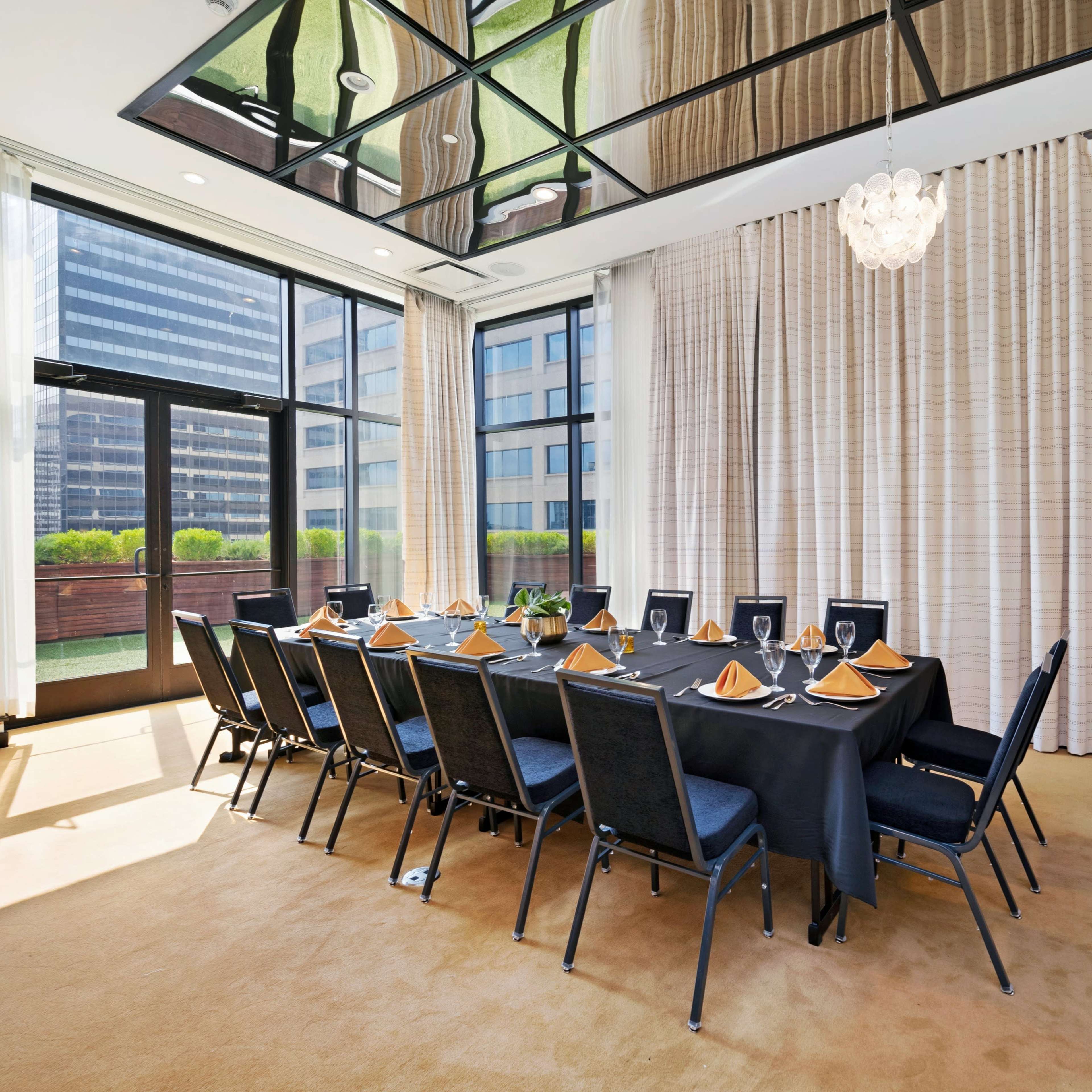 A conference room with a long table set for dining, surrounded by large windows and floor-to-ceiling curtains.