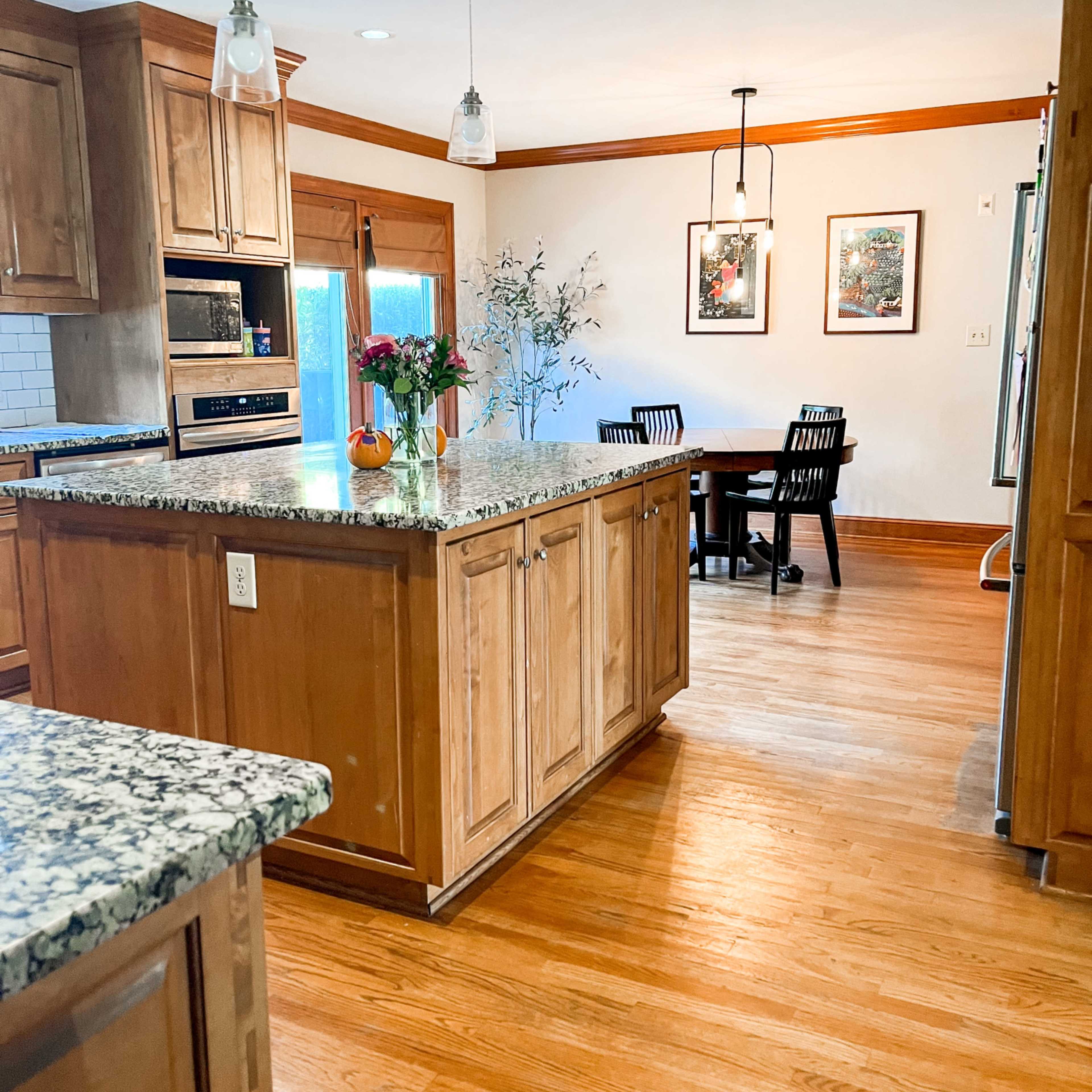 A spacious kitchen with wooden cabinets, a granite island, and a dining area featuring a round table and four black chairs.