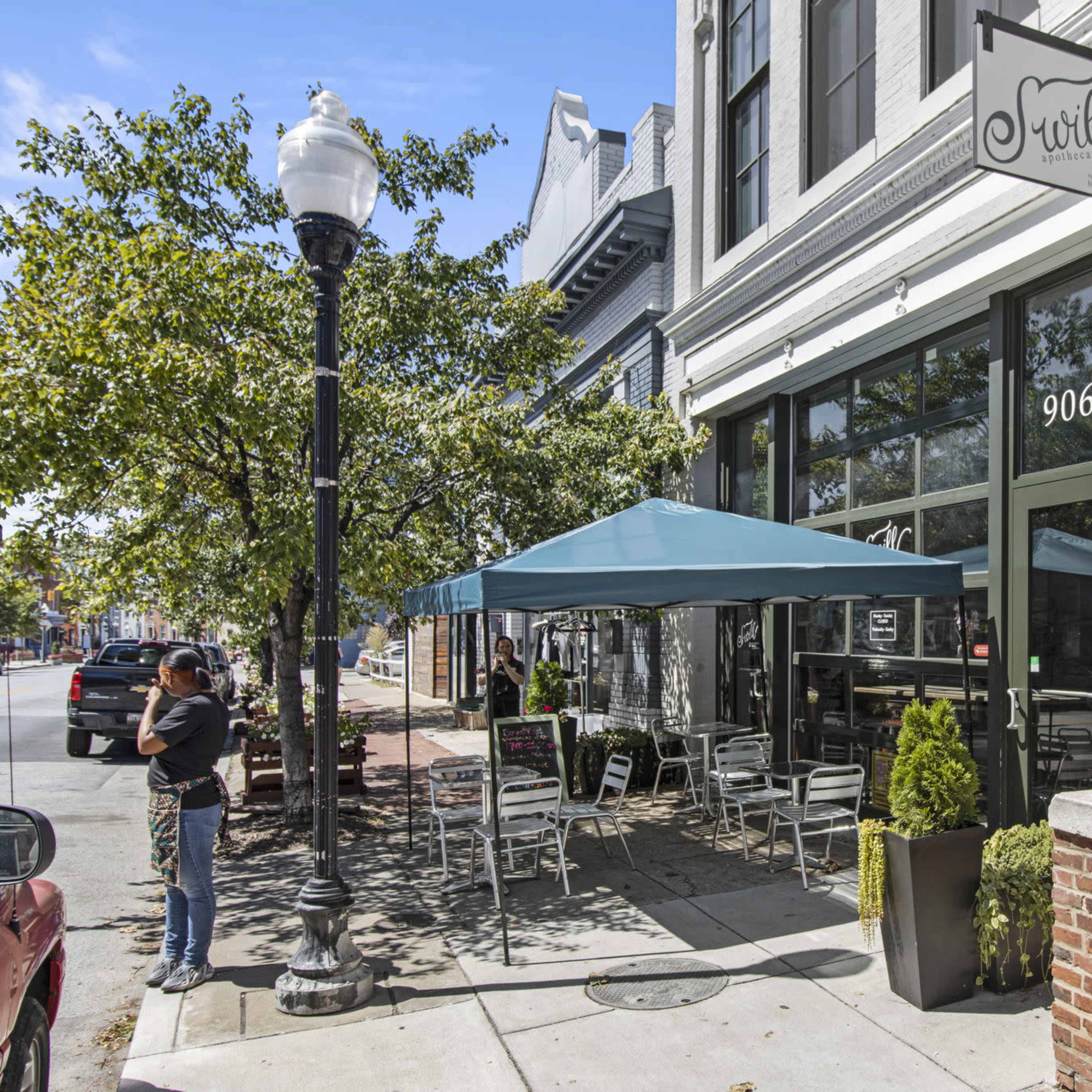 A café with outdoor seating under a blue canopy, located at 906 on a street lined with trees and buildings.