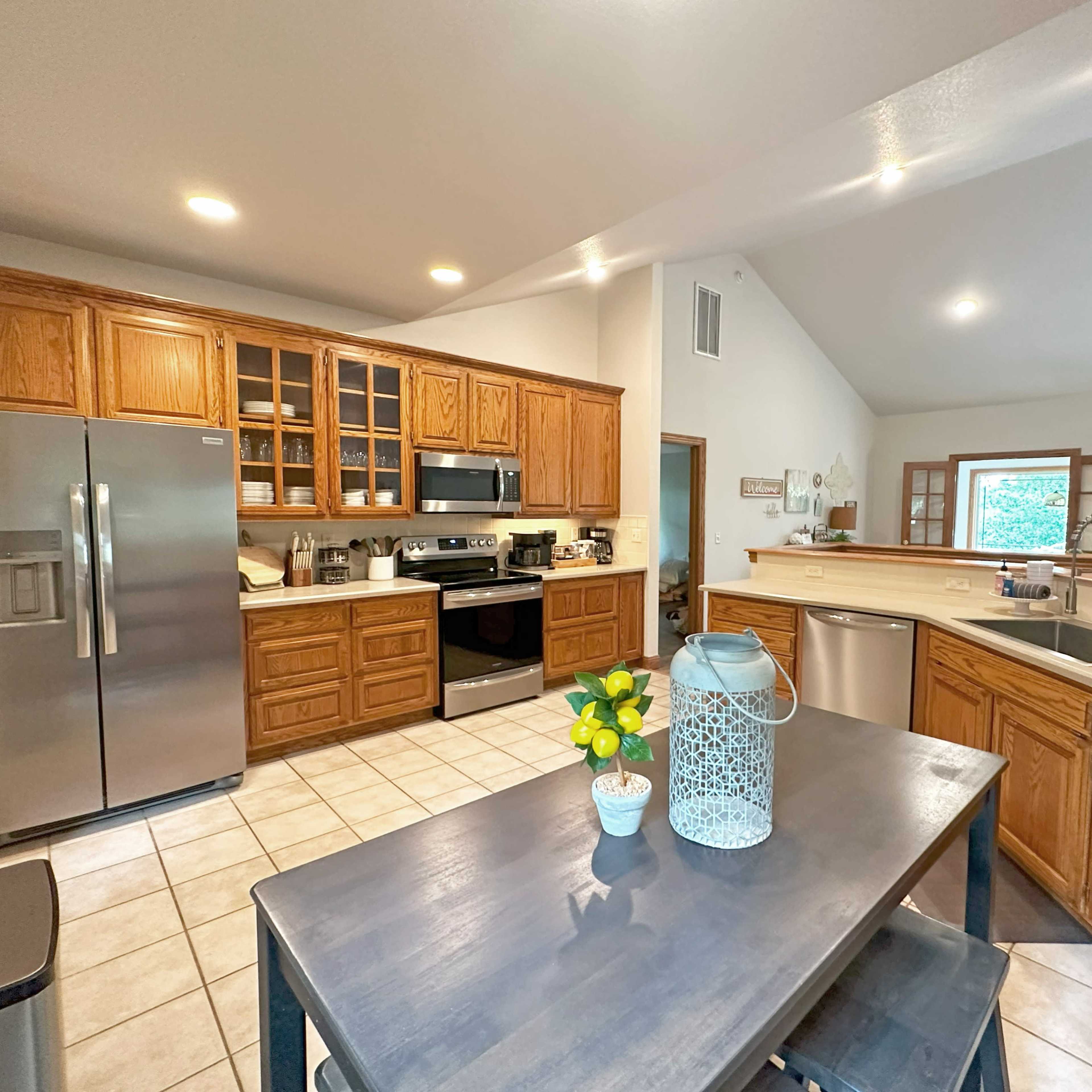 A spacious kitchen features wooden cabinets, stainless steel appliances, and a centrally placed dining table with a vase of flowers.