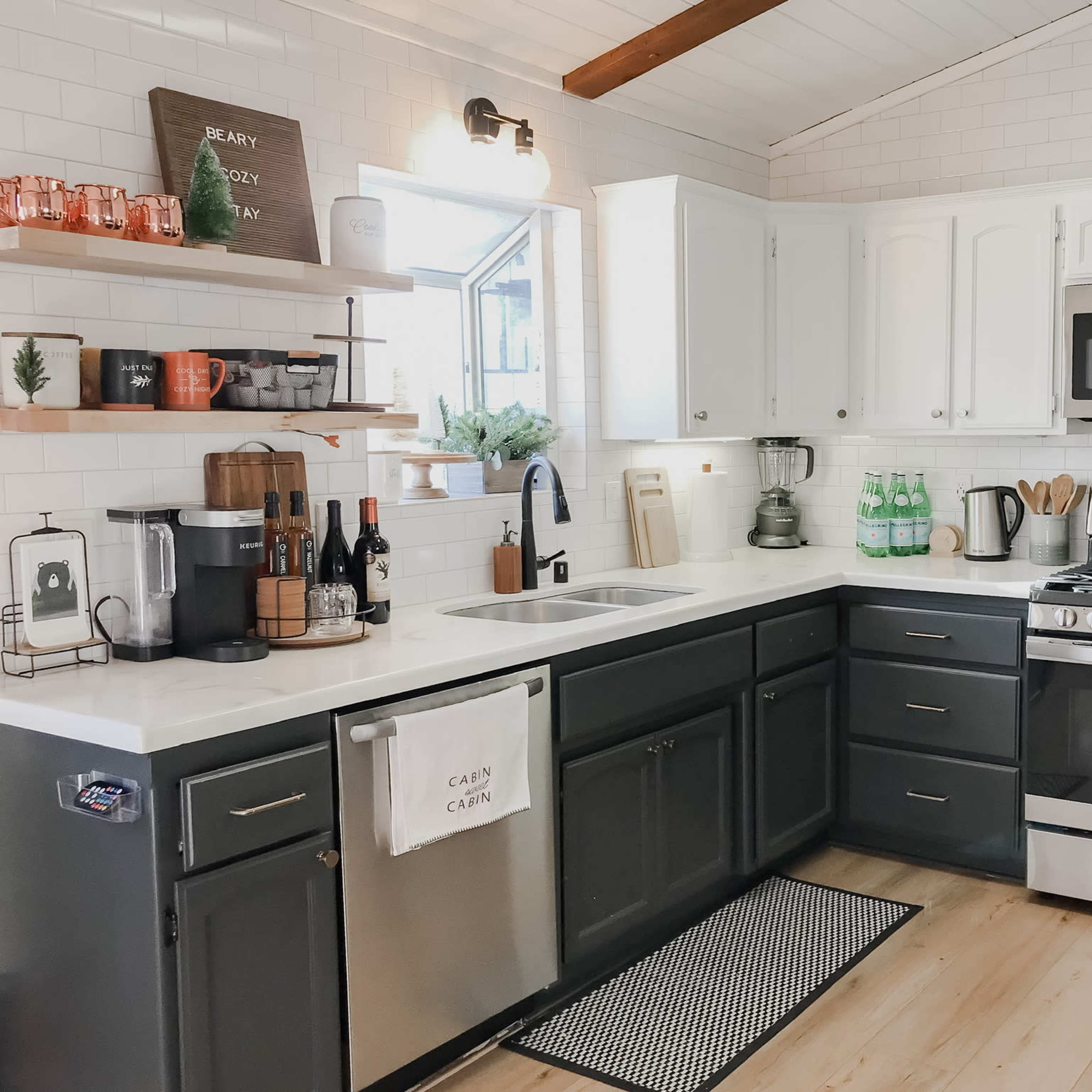 A modern kitchen with white cabinets, a stainless steel stove, and a gray island, featuring various kitchen appliances and decorative items on the shelves.