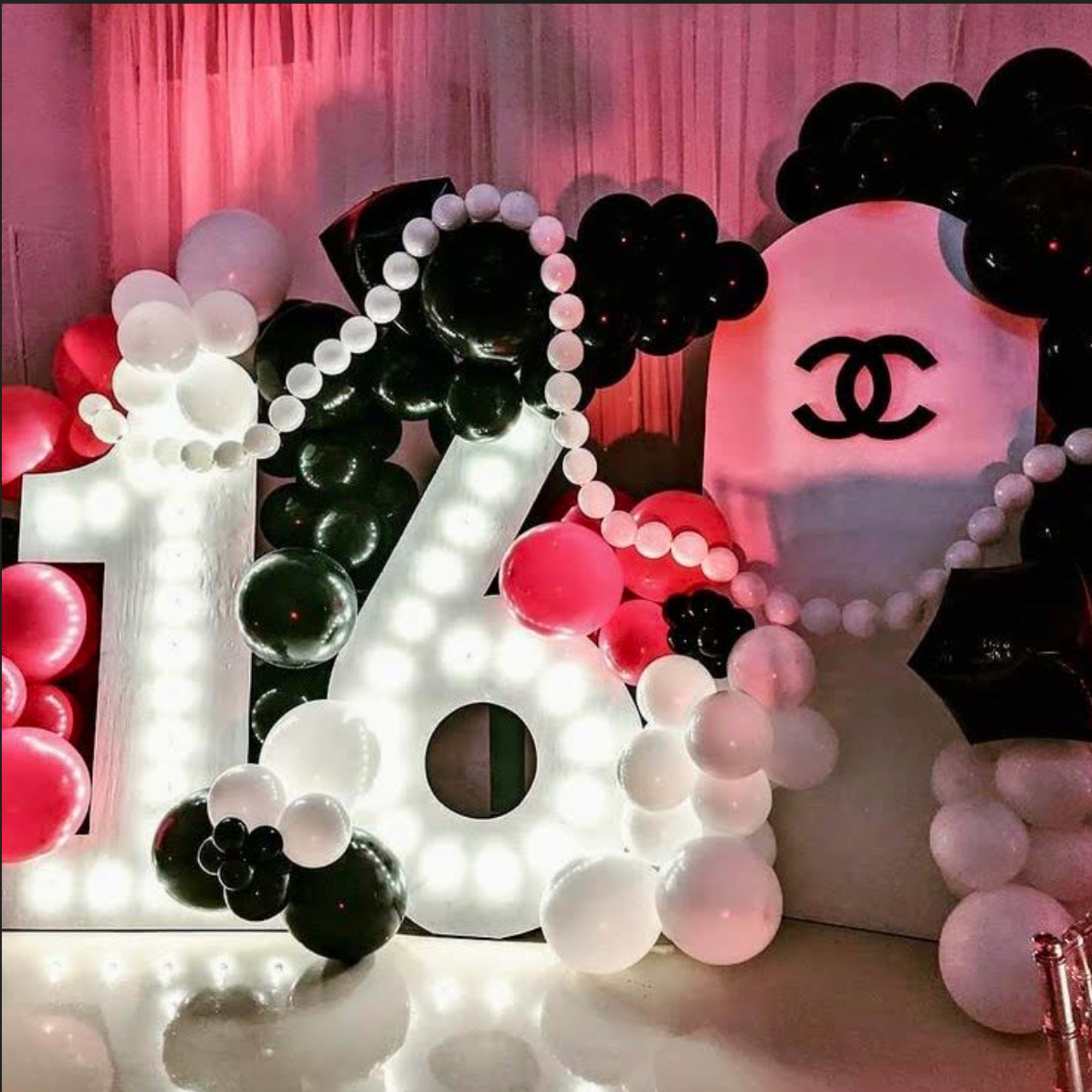 A large, illuminated "16" made of balloons, surrounded by black and white balloons, and displays a Chanel logo in the background.