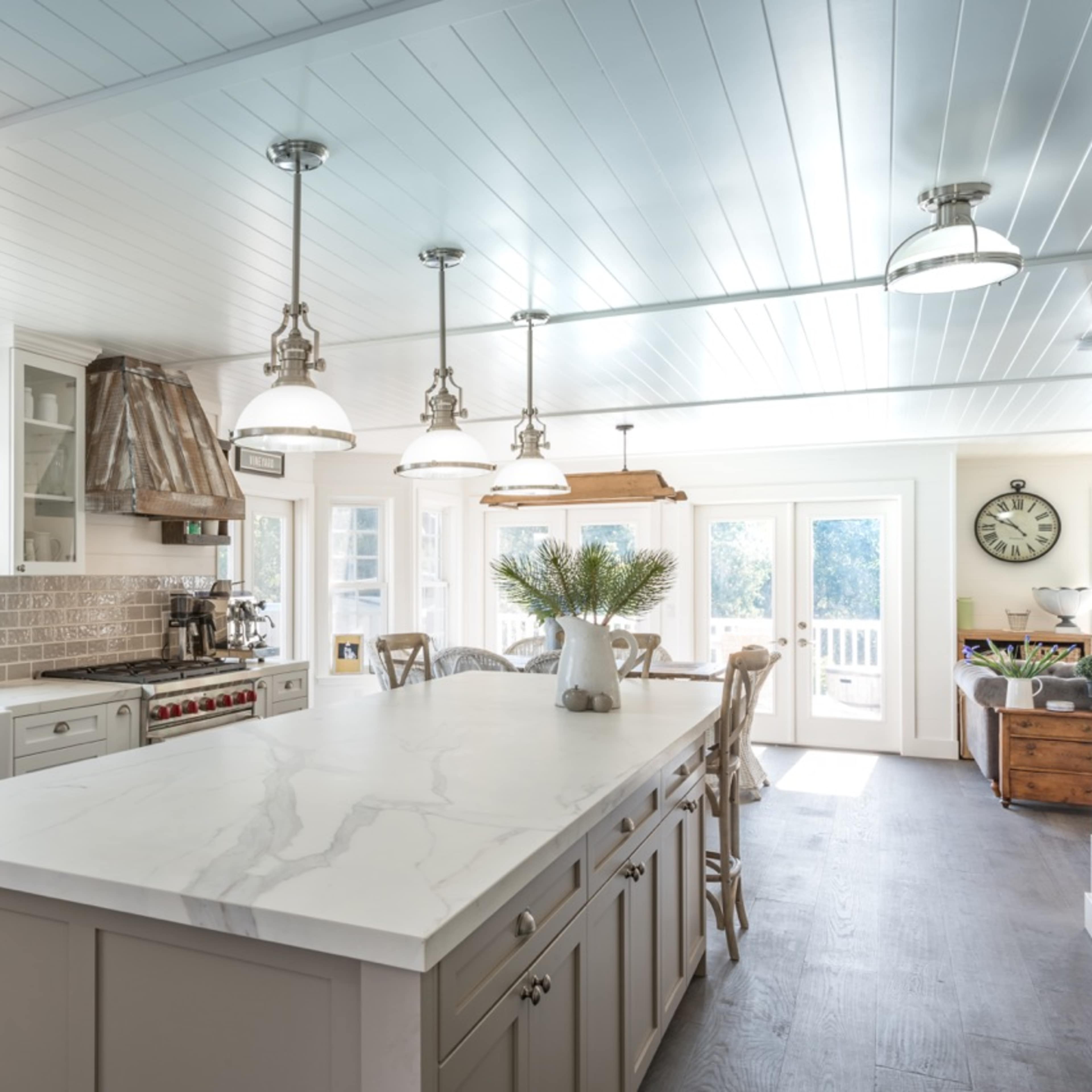 A modern kitchen features a large island with marble countertops, stainless steel appliances, and natural light coming through multiple windows.