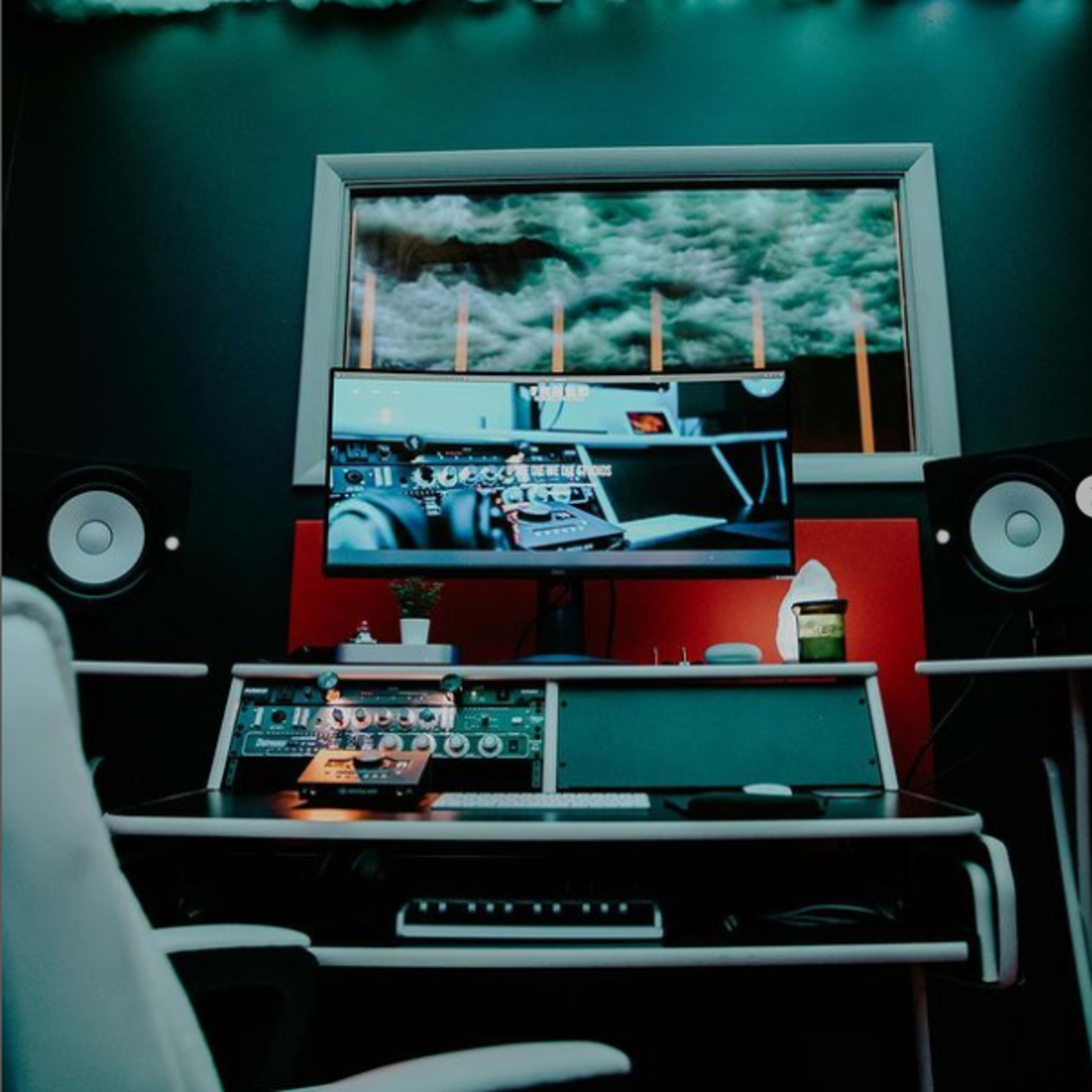 A music production studio with a large monitor displaying audio software, flanked by speakers, under a ceiling decorated to resemble clouds.