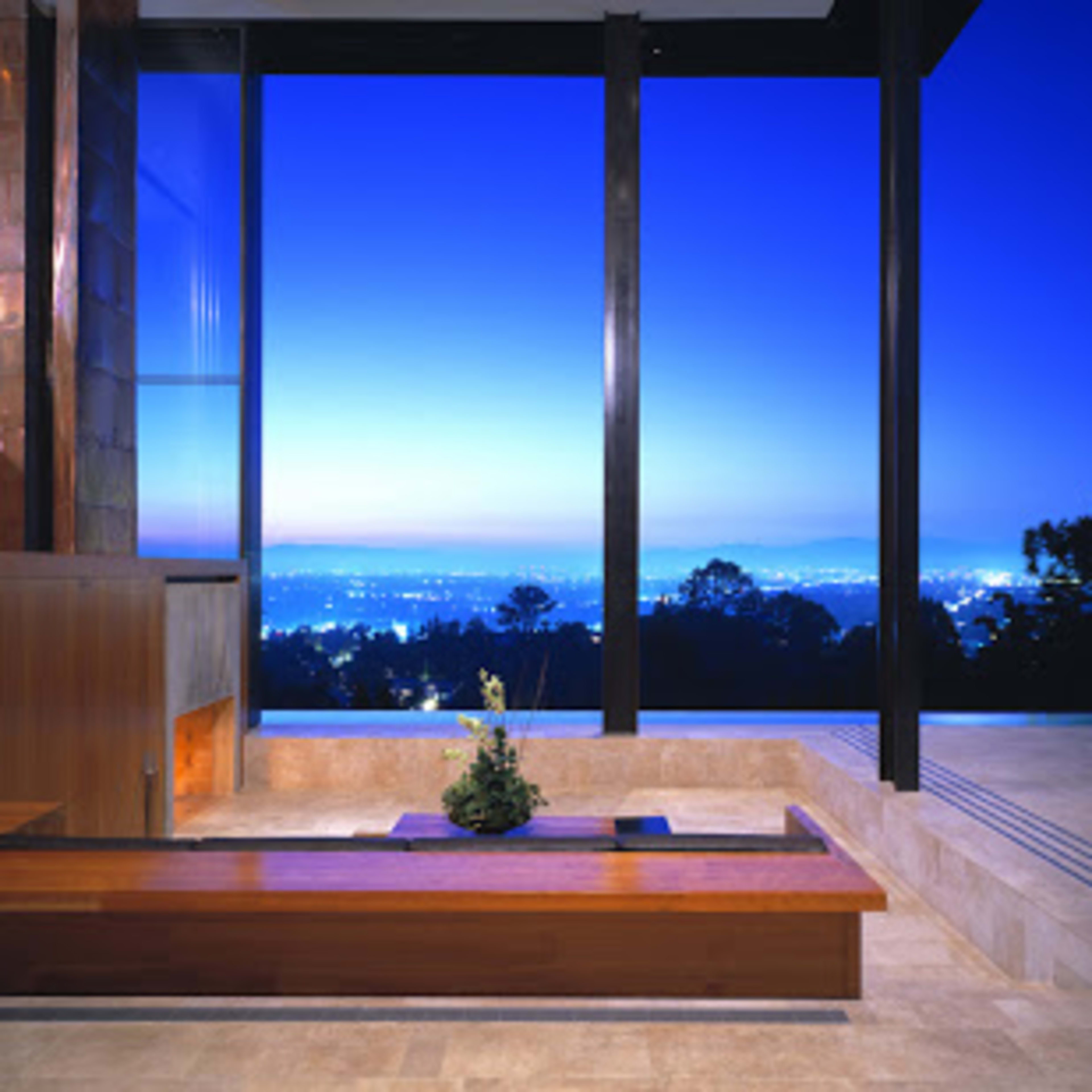 A modern indoor space with large glass windows overlooking a city skyline at twilight.