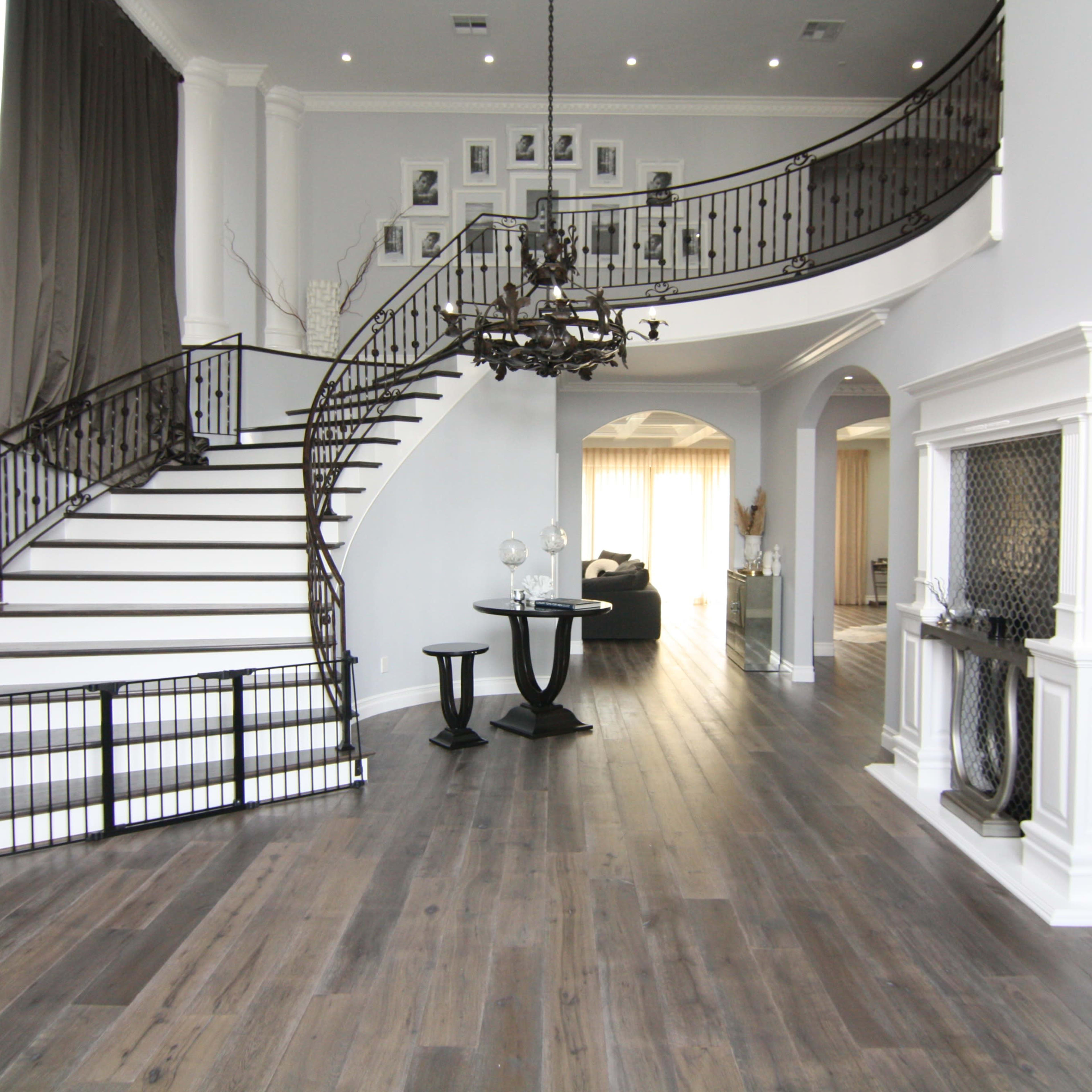 A spacious, modern foyer featuring a curved staircase with a wrought-iron railing, a chandelier, and a seating area.