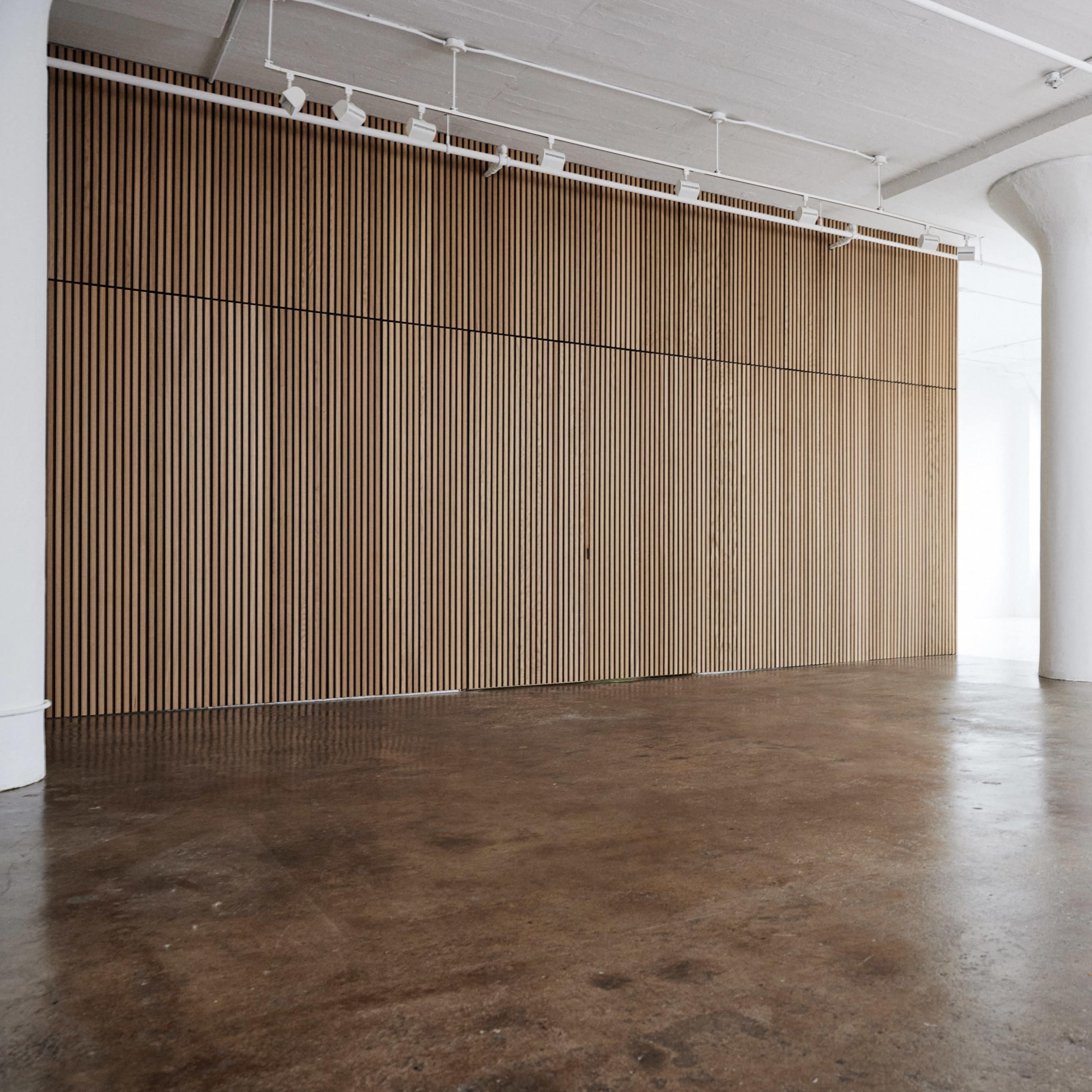 A spacious, minimalist interior featuring a wooden wall with vertical slats and a concrete floor.