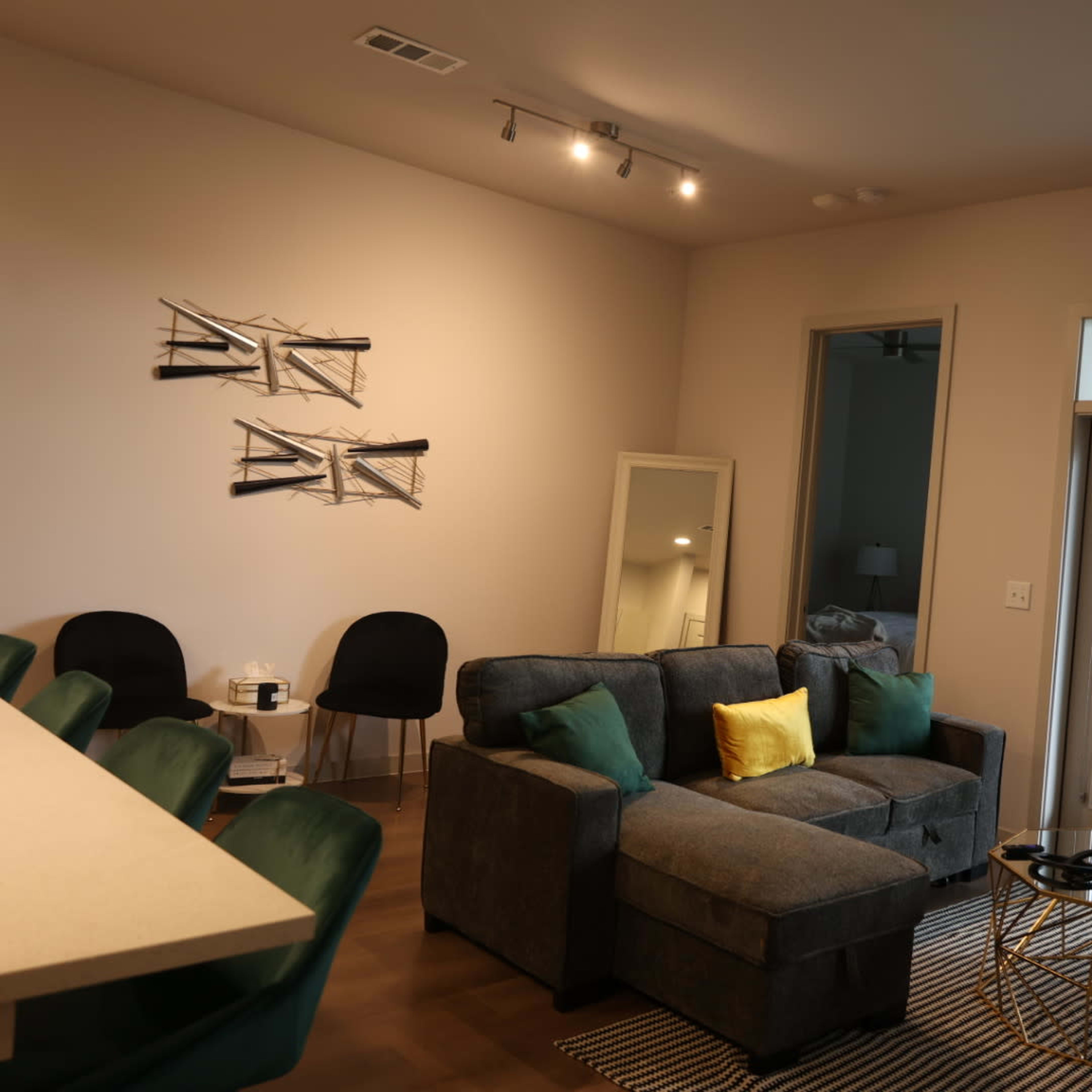 A modern living room features a gray sectional sofa with green and yellow pillows, a round coffee table, and large doors leading to an outdoor space.