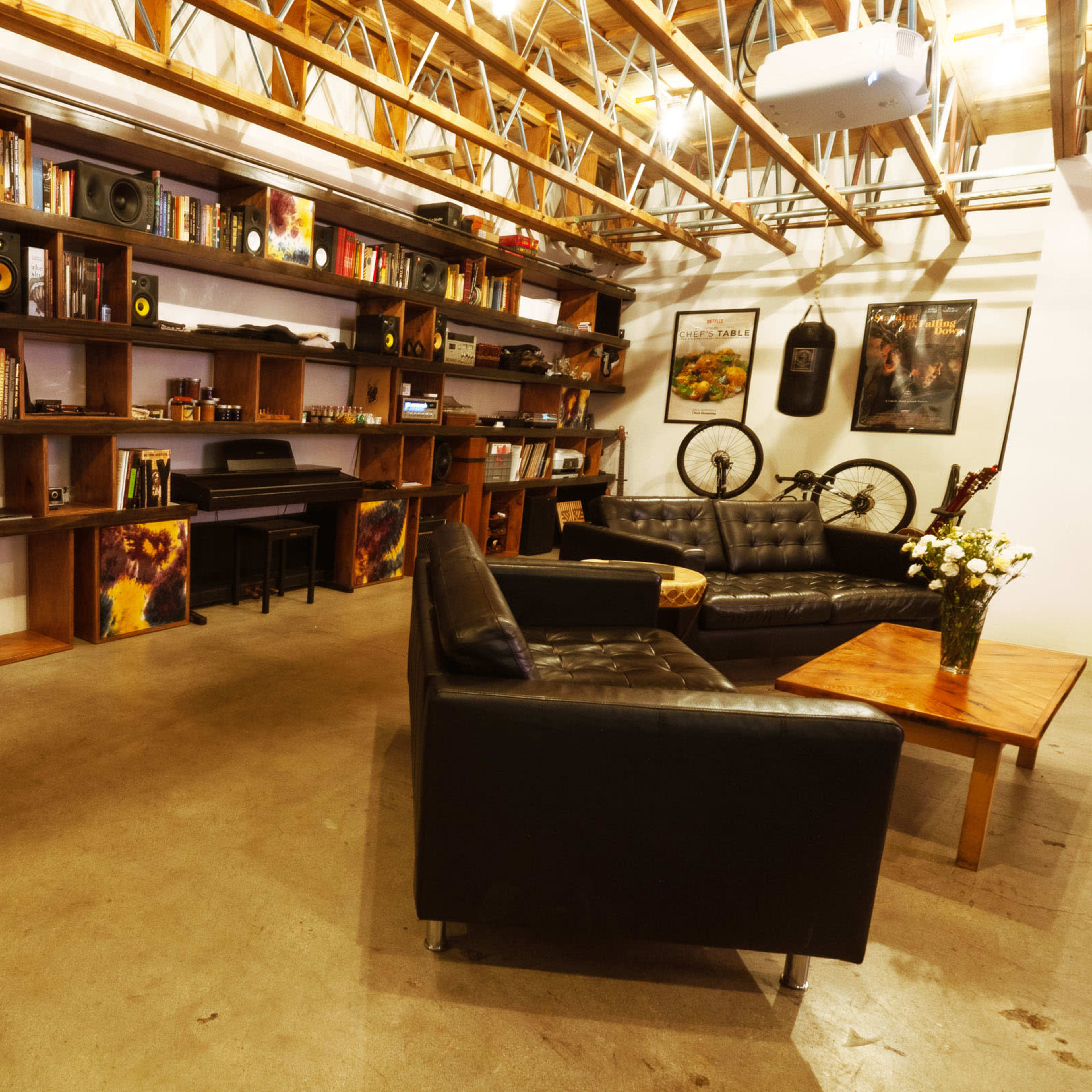 A modern interior space with a black leather couch, a wooden coffee table, bookshelves filled with books, and a ladder leaning against the shelves.