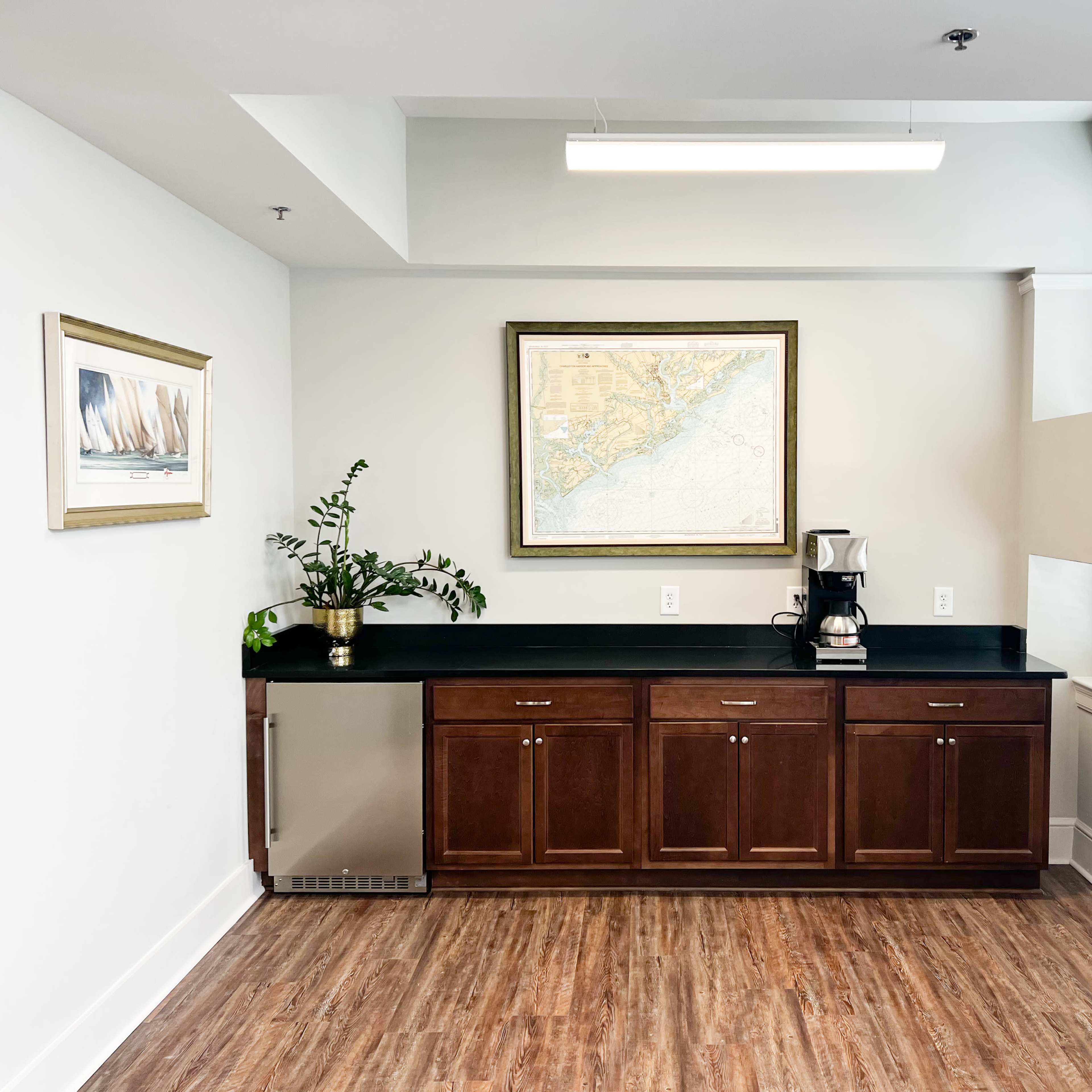A kitchenette features dark cabinets under a wall-mounted map, with a coffee machine and a potted plant on the counter.