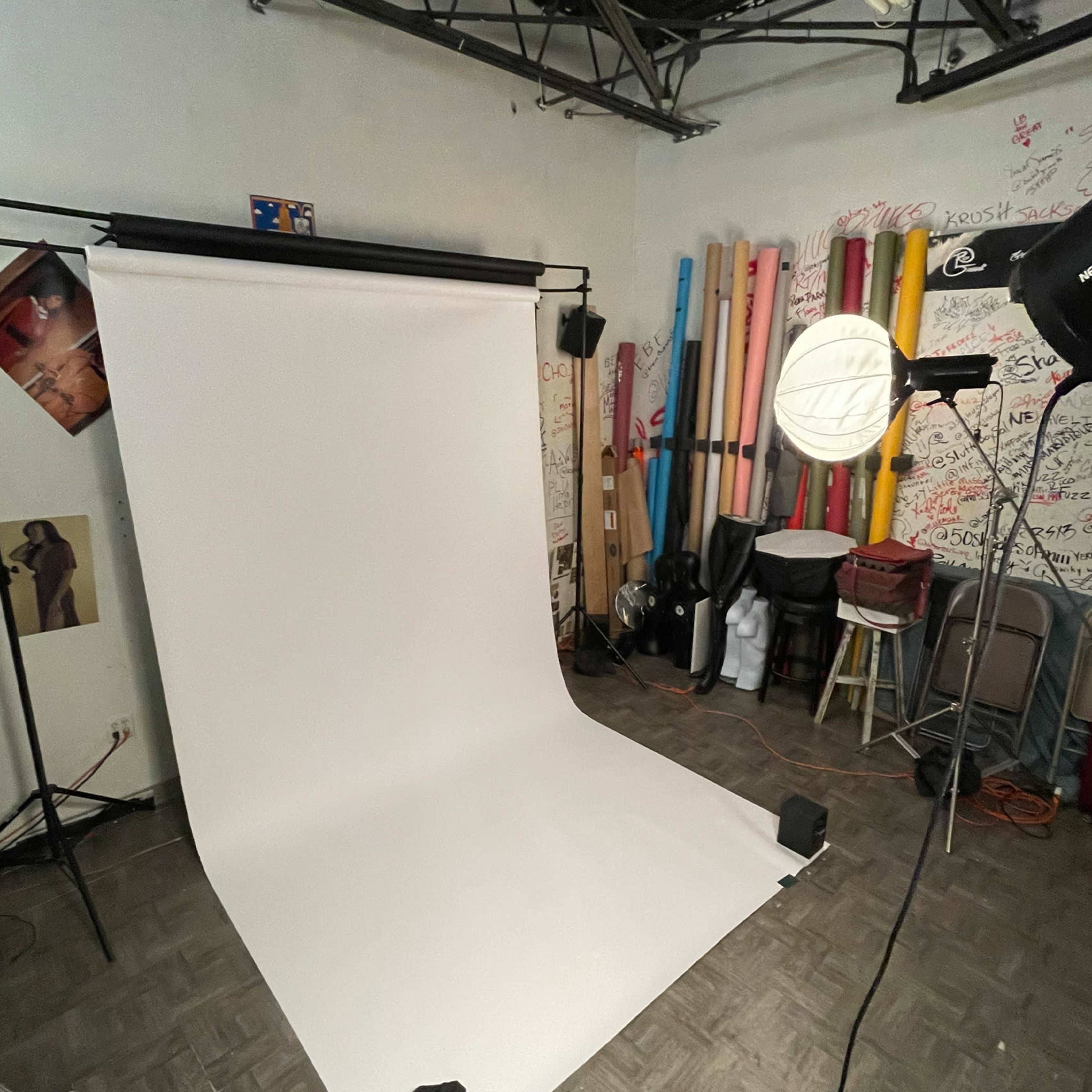 A photography studio setup with a white backdrop, lighting equipment, and various props and materials in the background.