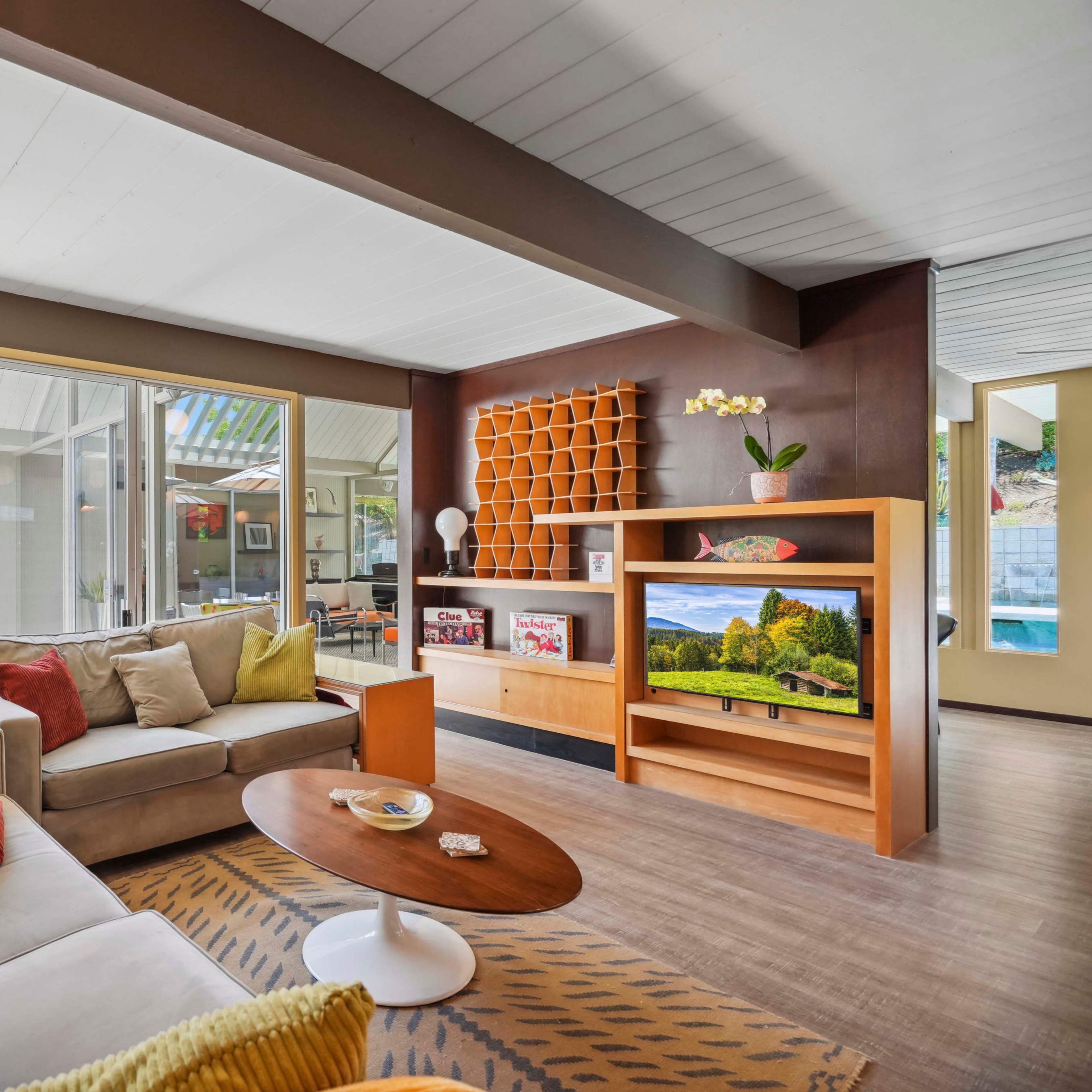 A modern living room featuring a beige couch, a round coffee table, and large windows allowing natural light to enter.
