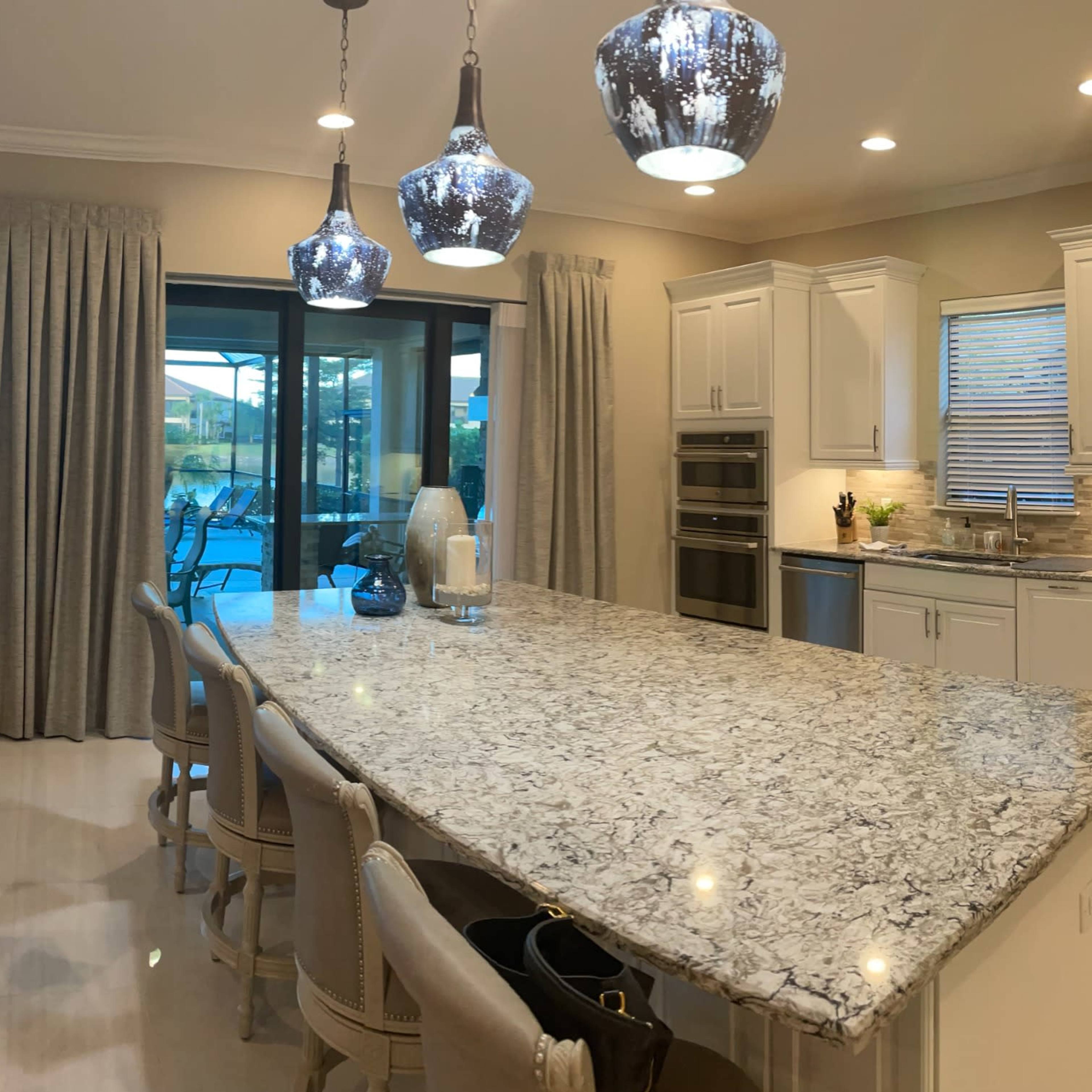 A modern kitchen features white cabinetry, granite countertops, stainless steel appliances, and pendant lighting, with an open view to a patio through large glass doors.