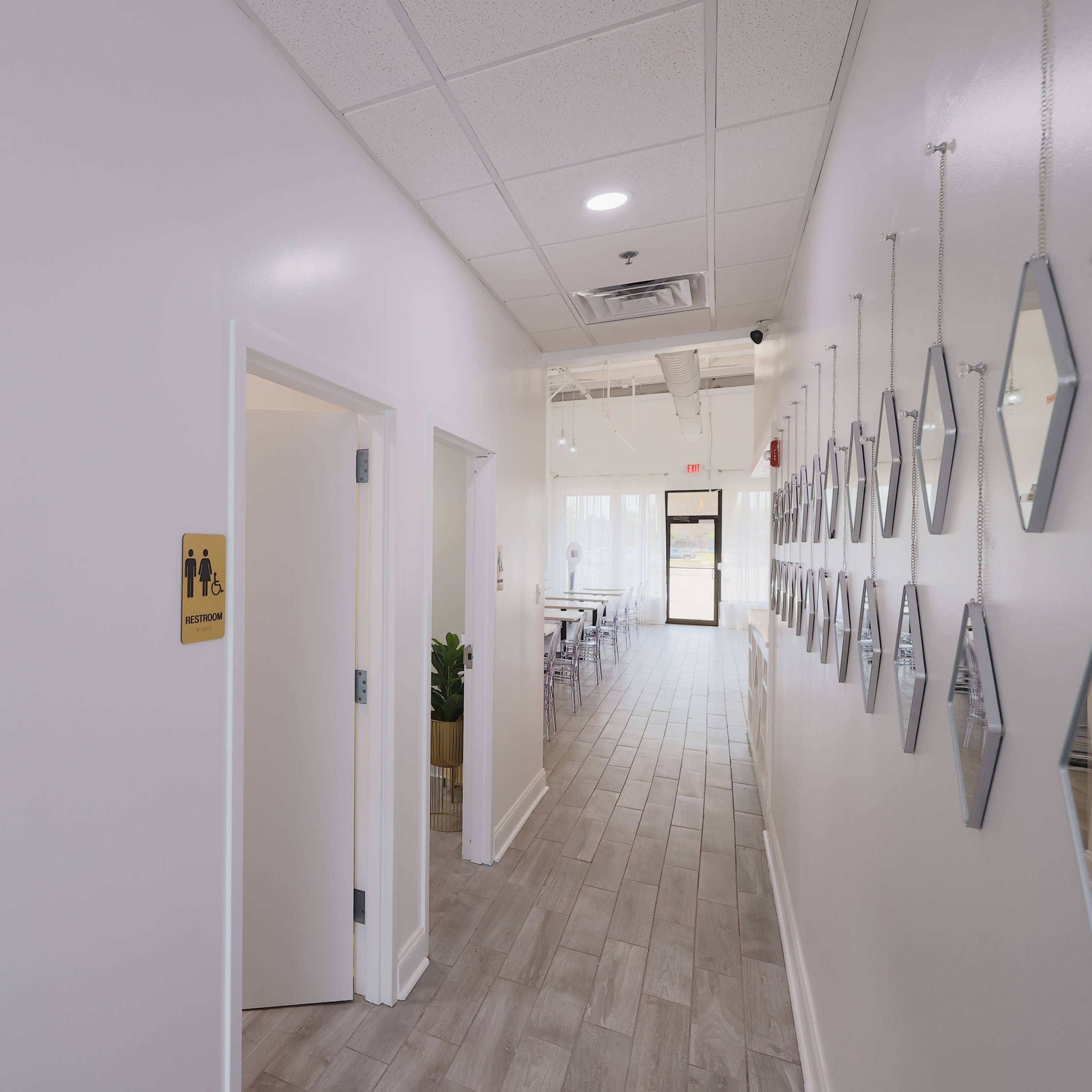 A hallway with a closed door on the left leading to a restroom and a series of mirrors lining the wall on the right.