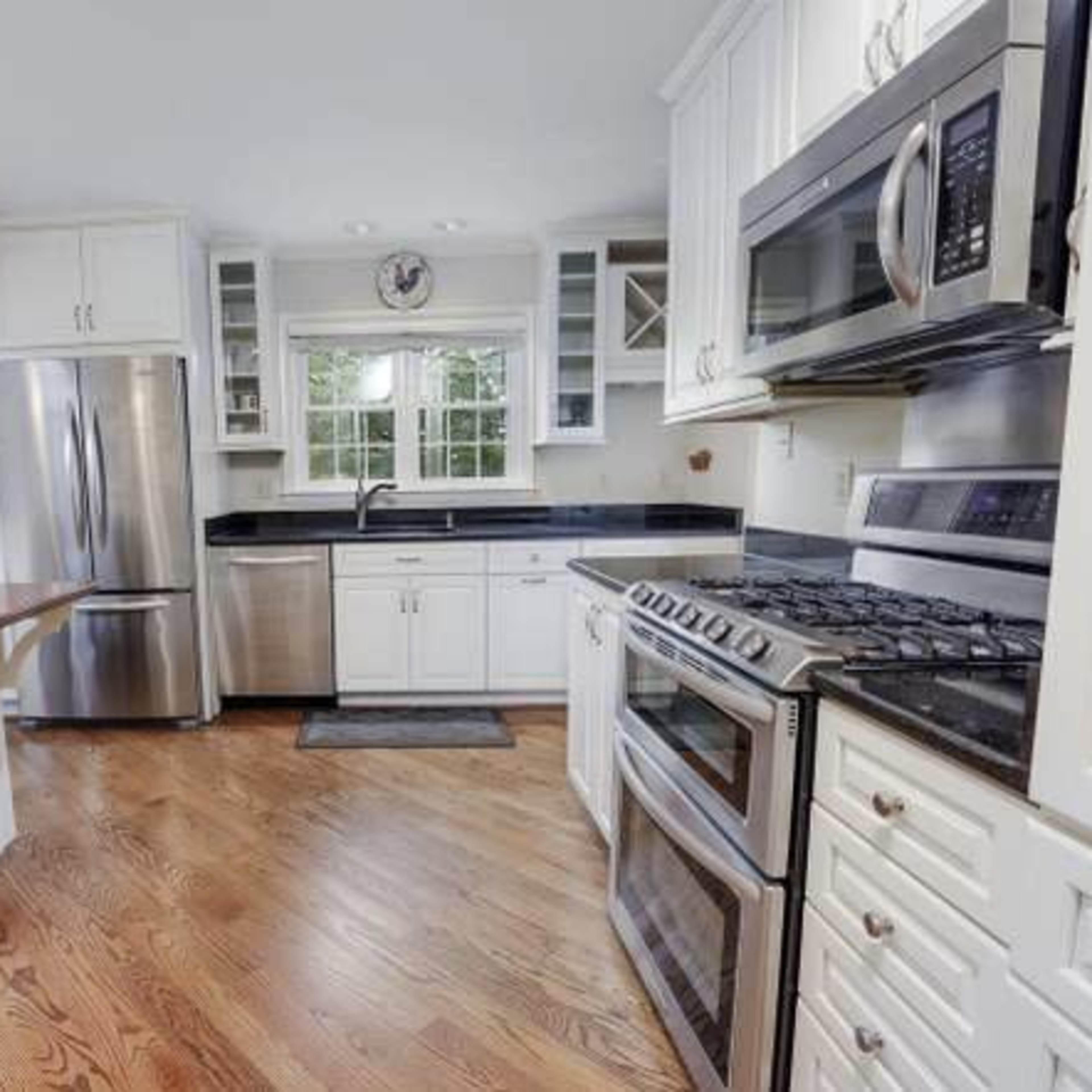 A modern kitchen features white cabinets, stainless steel appliances, and hardwood flooring.