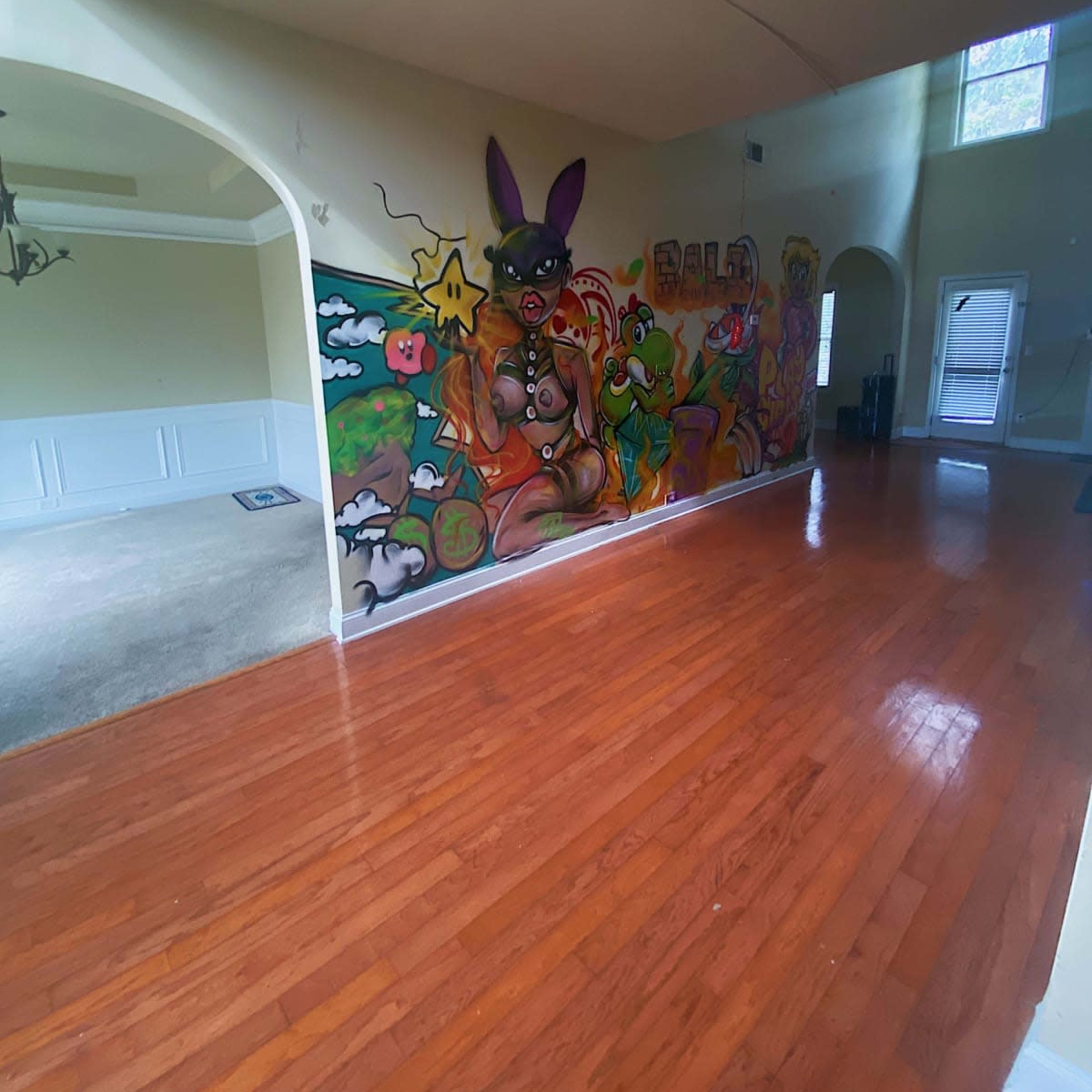 A spacious room with polished wooden floors and a wall decorated with colorful graffiti art.