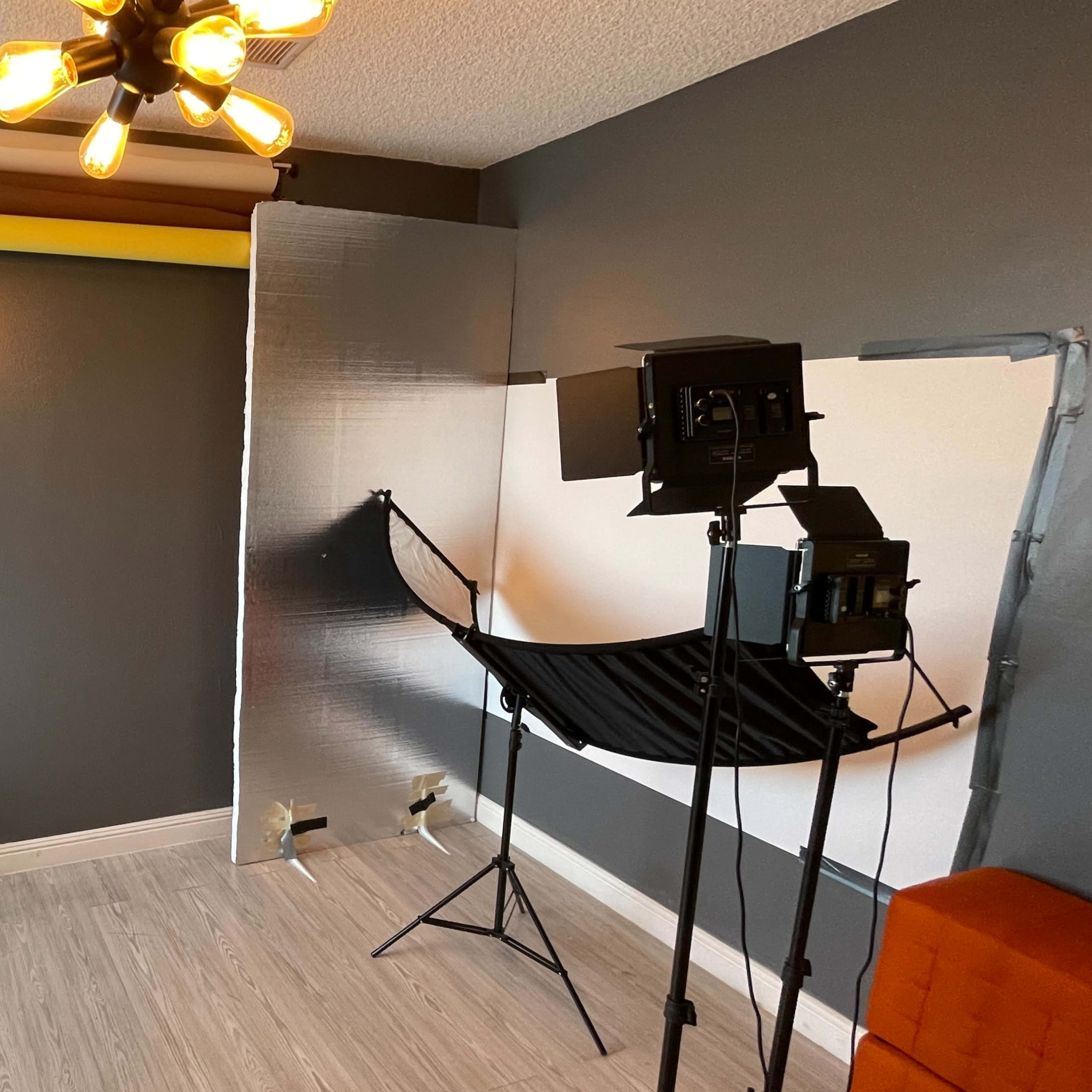 A photography studio setup featuring a stool, backdrop stands, and lighting equipment in a room with gray walls and various colored backdrop rolls.