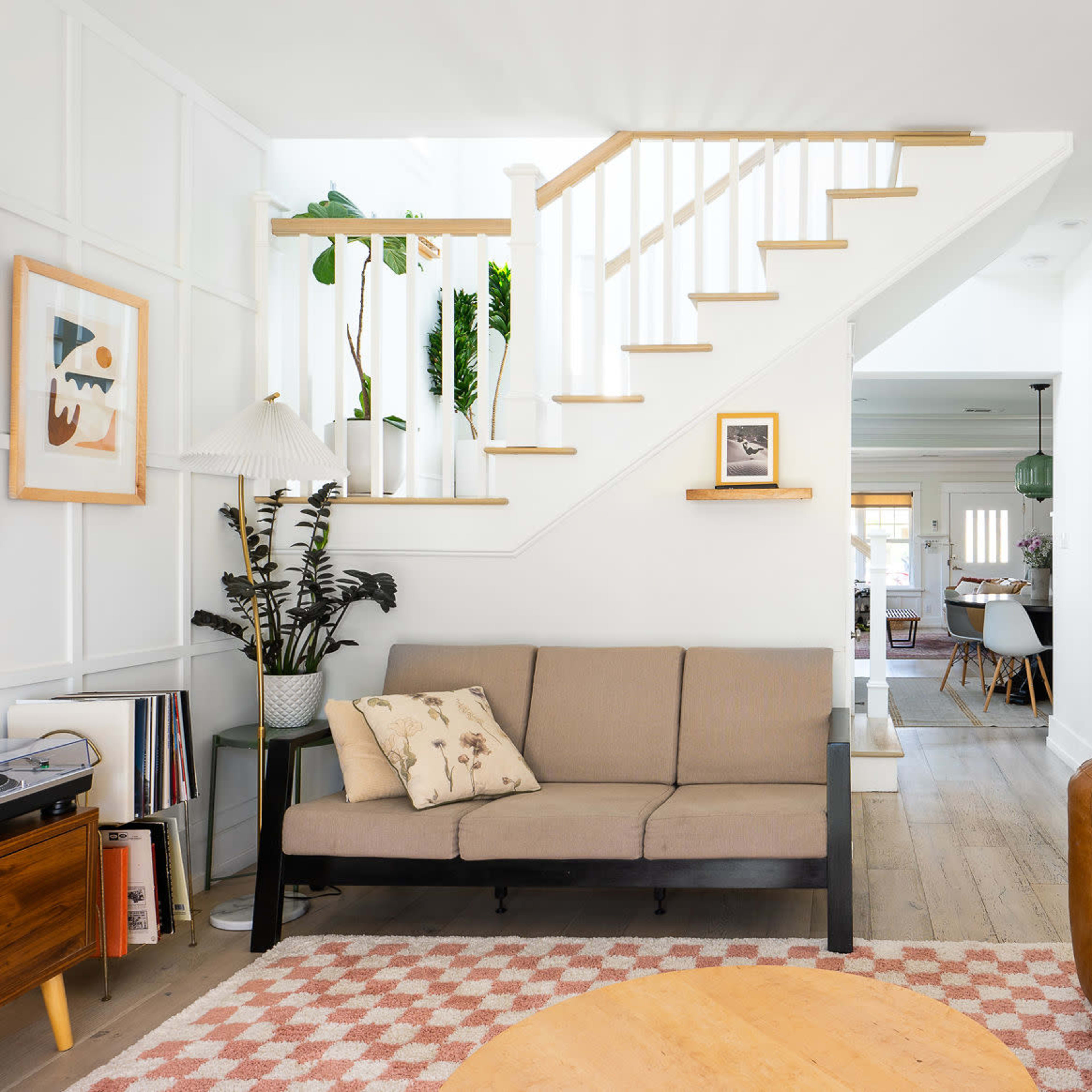 A bright living room featuring a brown couch, a beige loveseat, a round wooden coffee table, and a staircase in the background.