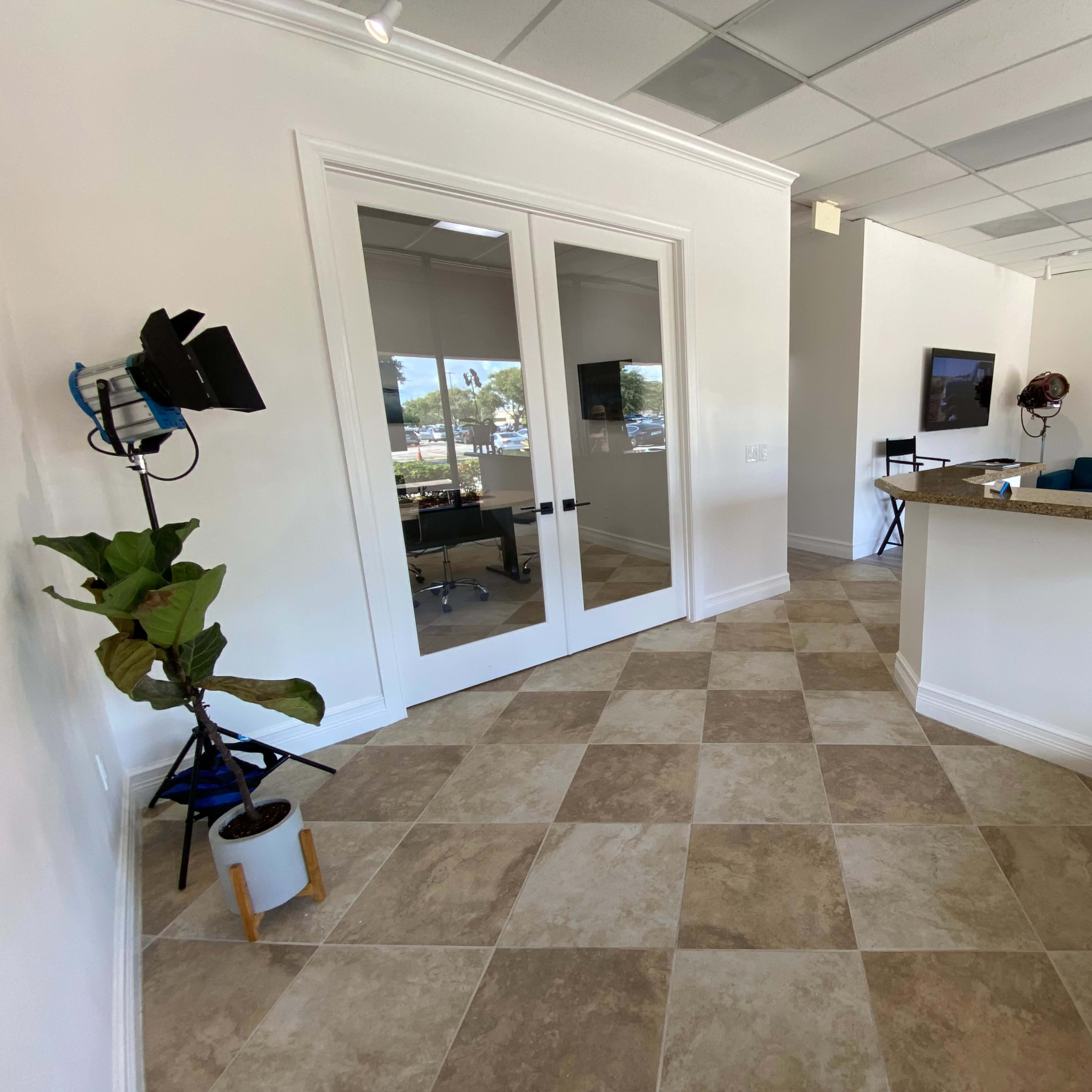 An office reception area with a tiled floor, a front desk, and glass double doors leading to another room.