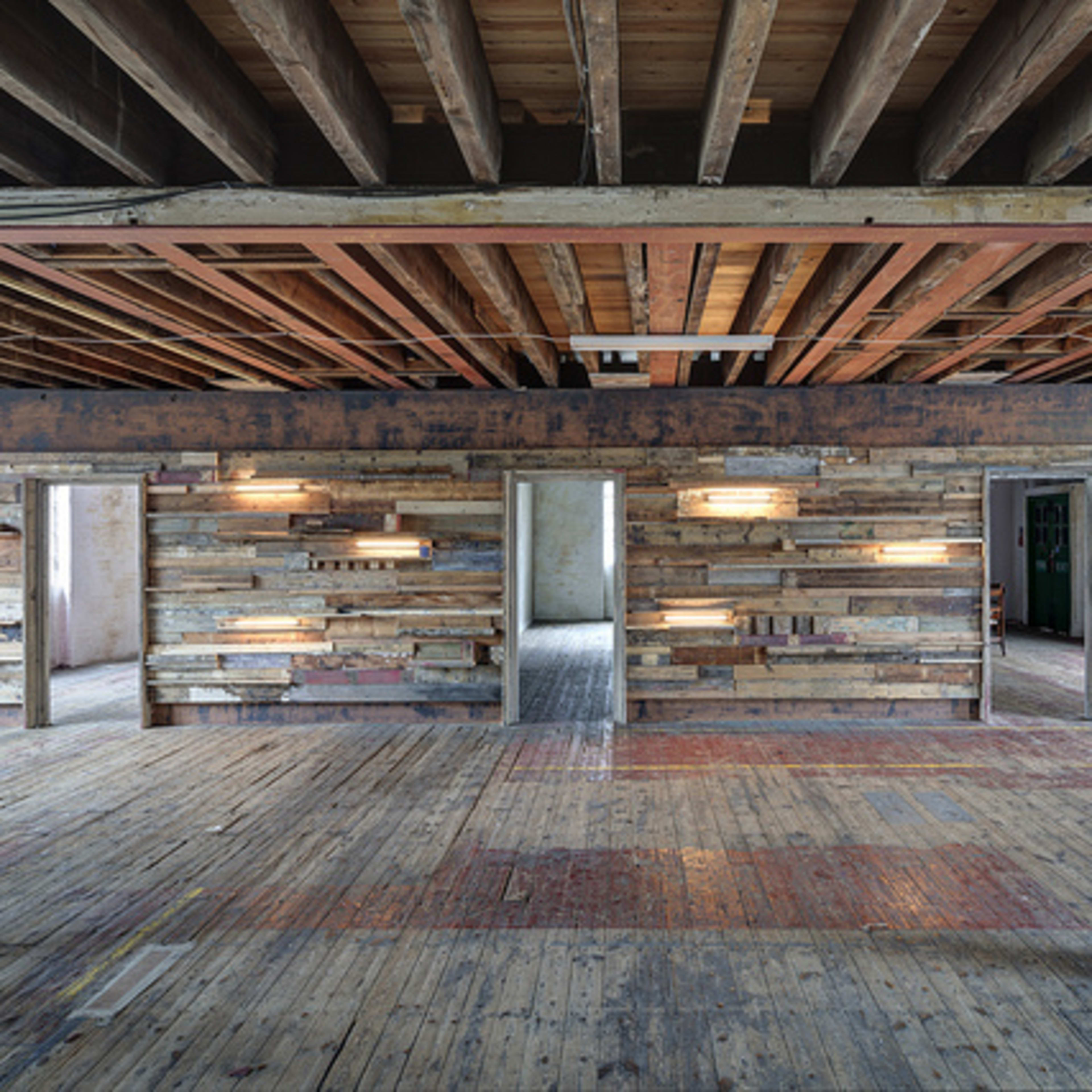 An open room with exposed wooden beams, wooden plank walls, and minimal furnishings.
