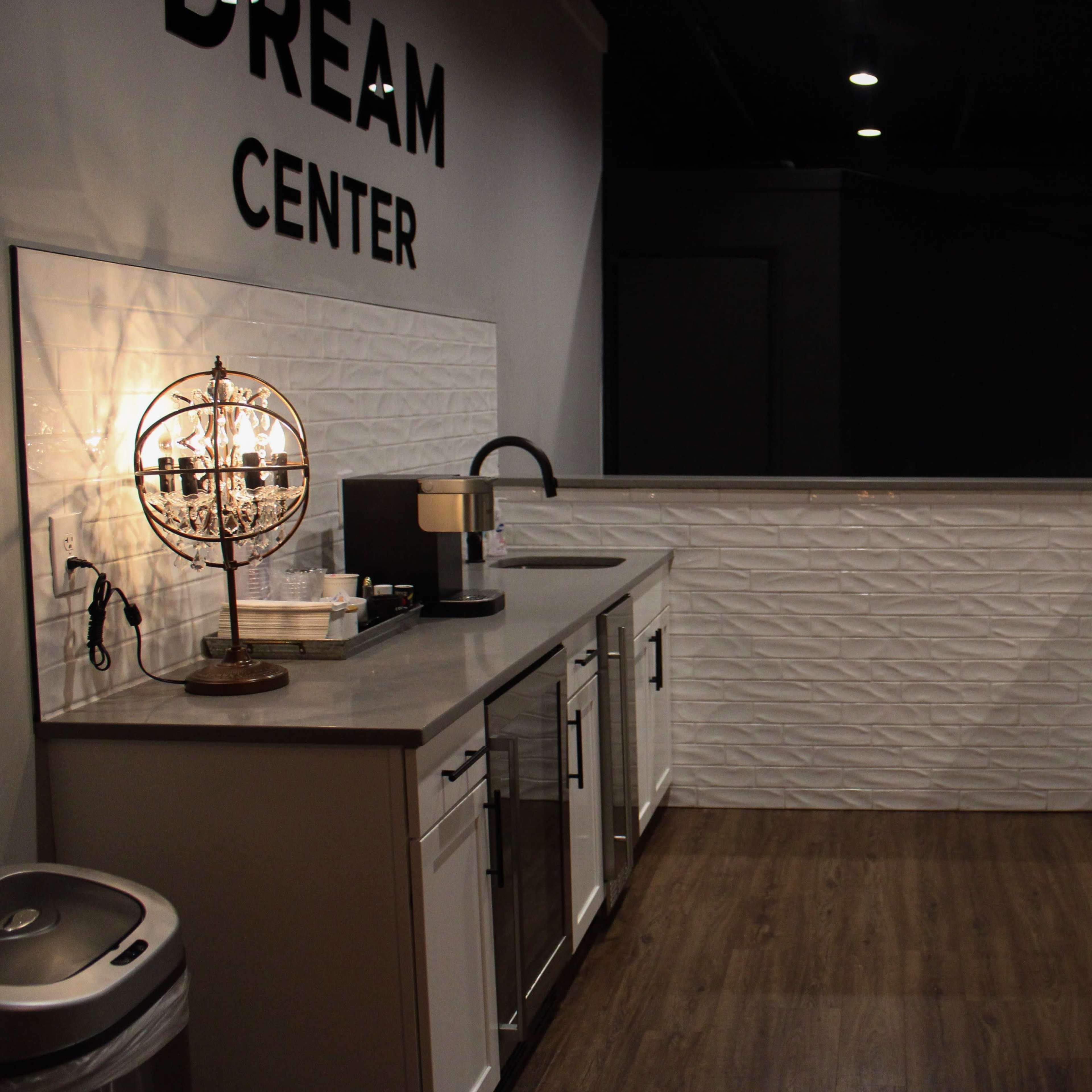 A modern kitchen space with white cabinetry, gray countertops, and a textured wall, labeled "DREAM CENTER."