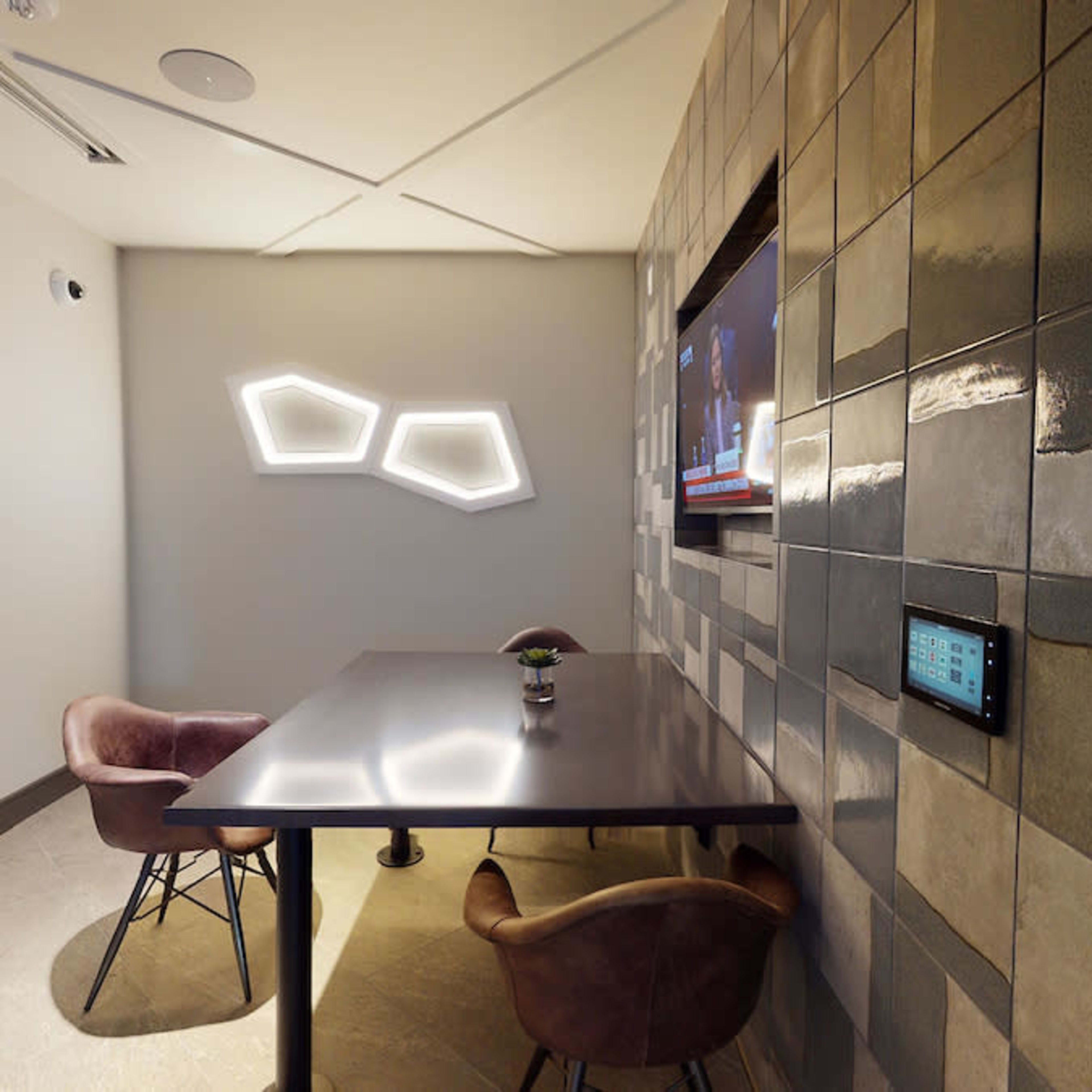 A small conference room features a table with two chairs, a wall-mounted television, and modern wall decor.