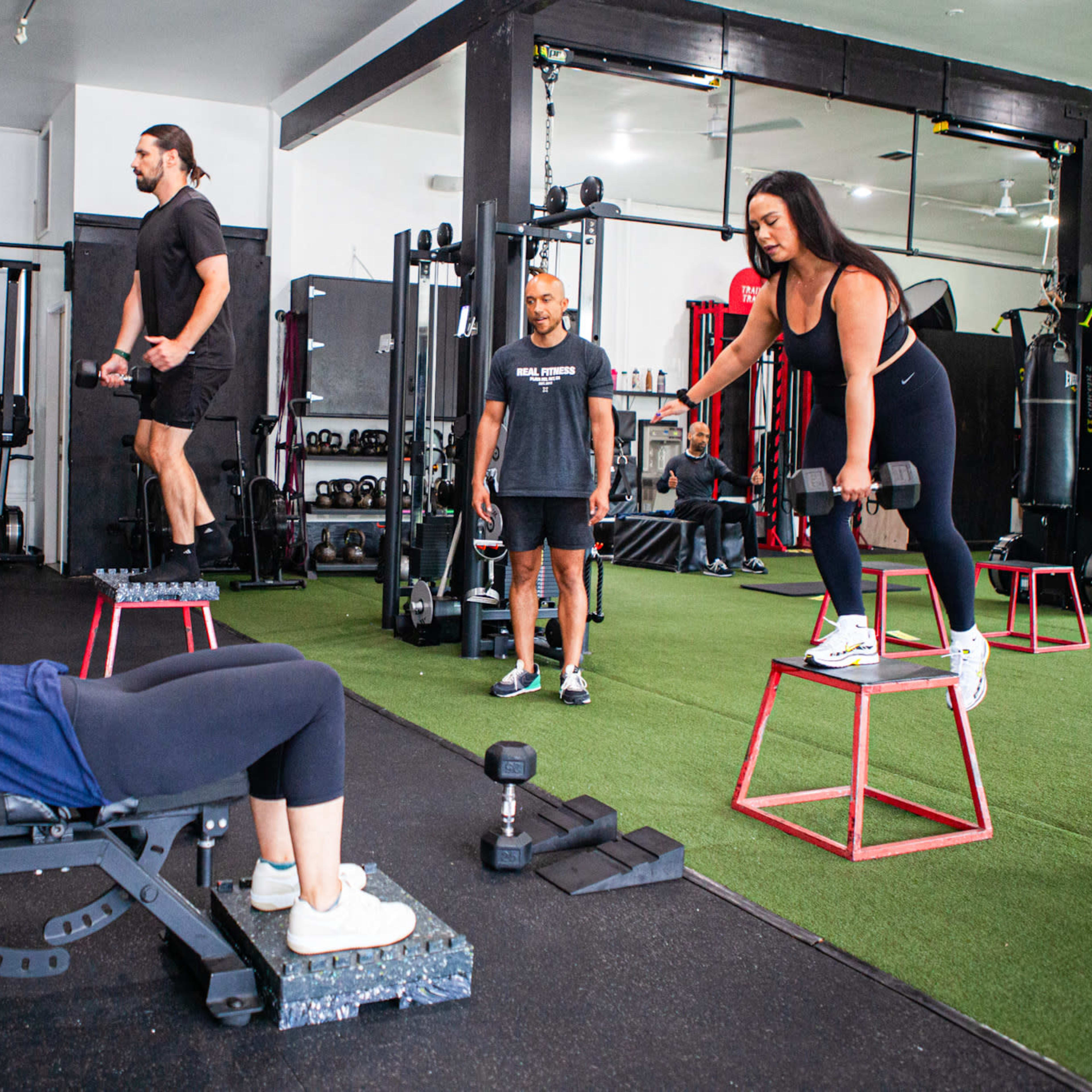 A group of four people engages in various weightlifting exercises in a gym setting.