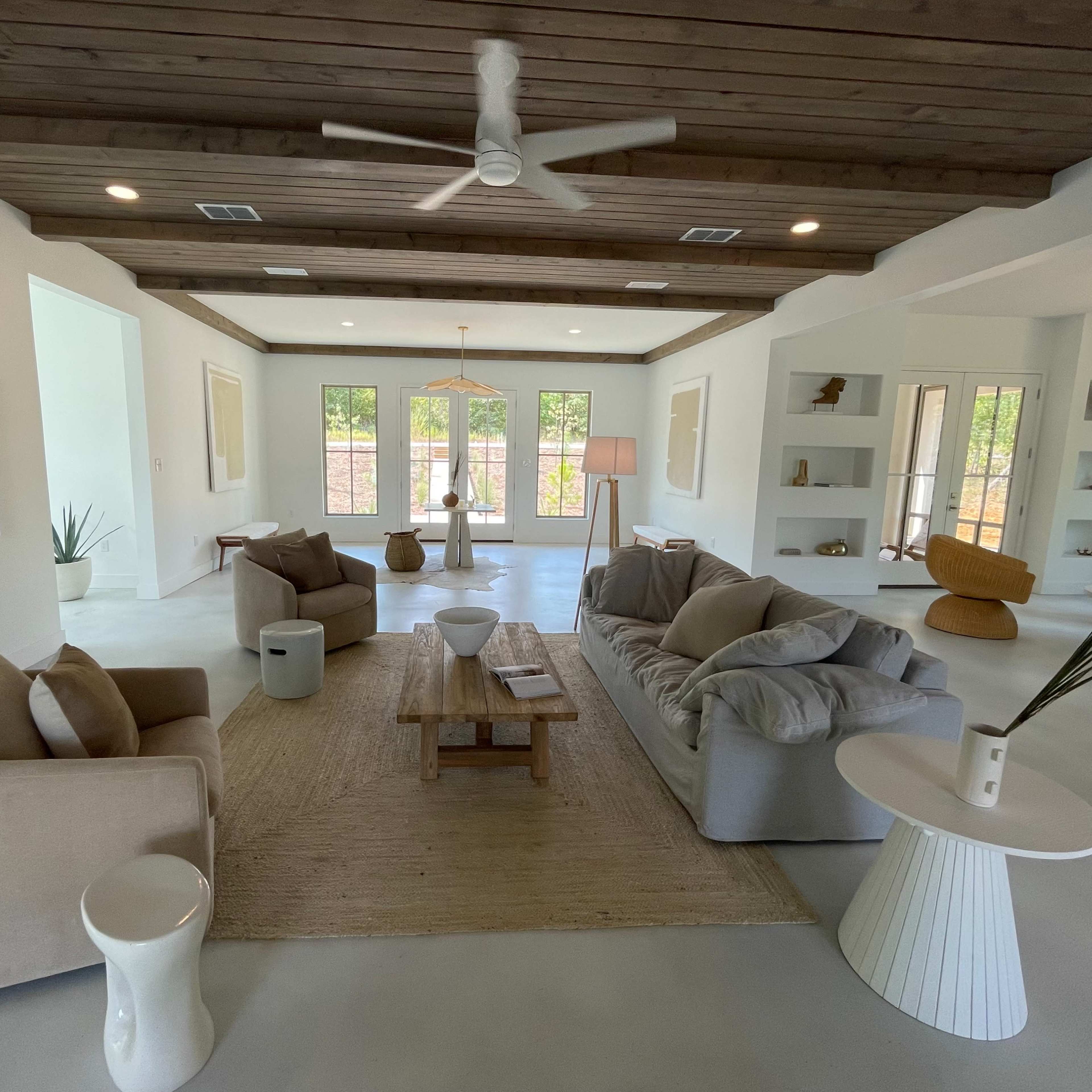 A spacious living room with a mix of modern furniture, including a gray sofa, beige armchairs, a wooden coffee table, and decorative items on shelves.