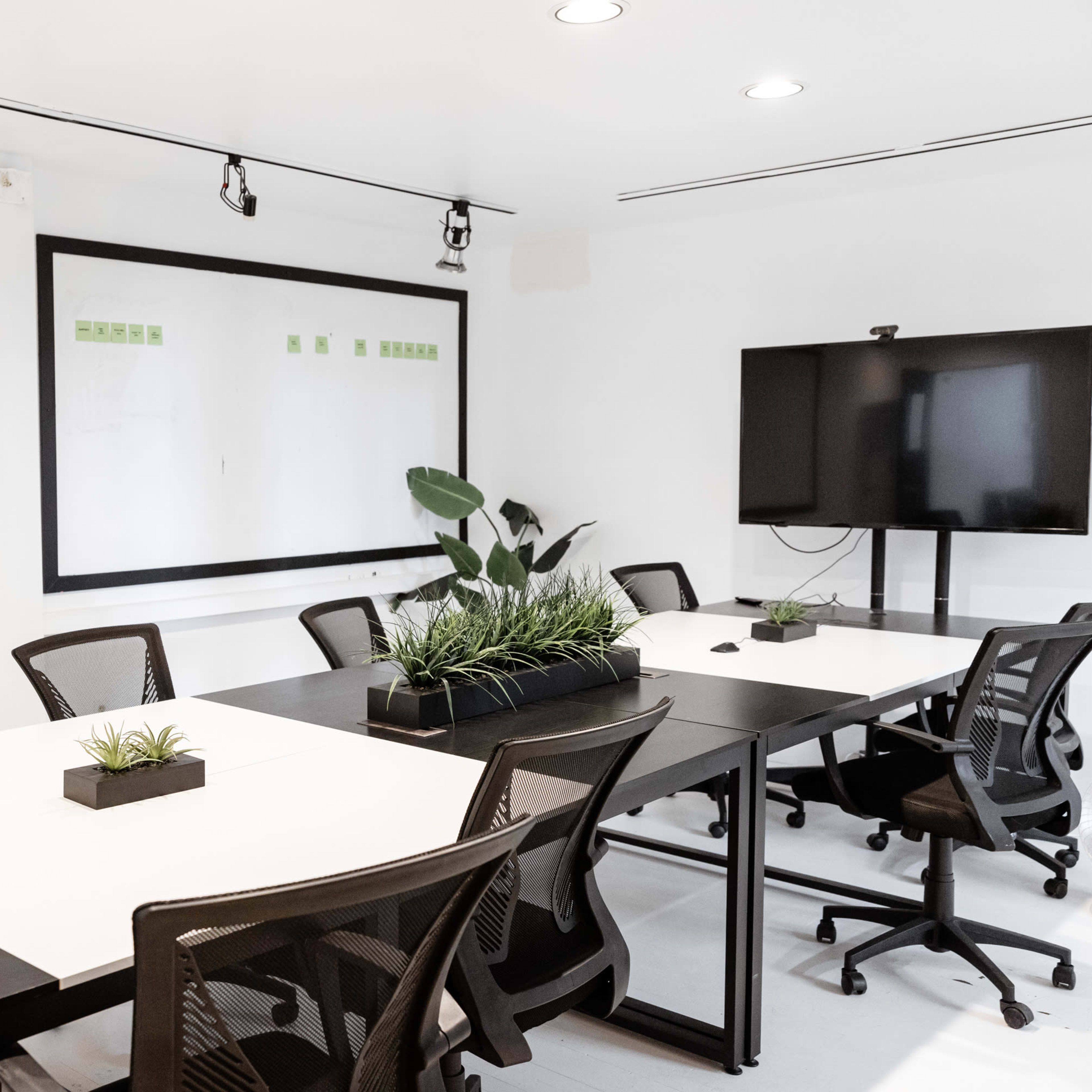 A modern conference room features a large table surrounded by chairs, whiteboards on the walls, and a TV mounted in the corner.