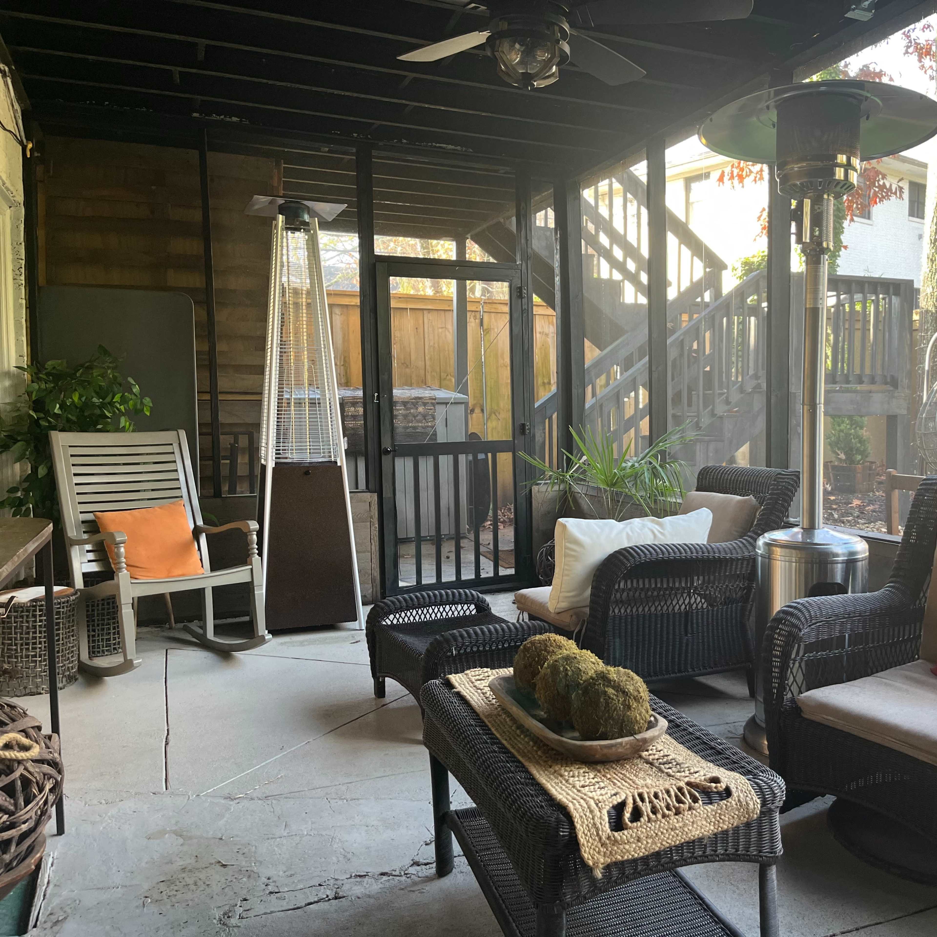 A covered patio area with wicker furniture, a heating lamp, and steps leading to a higher level.