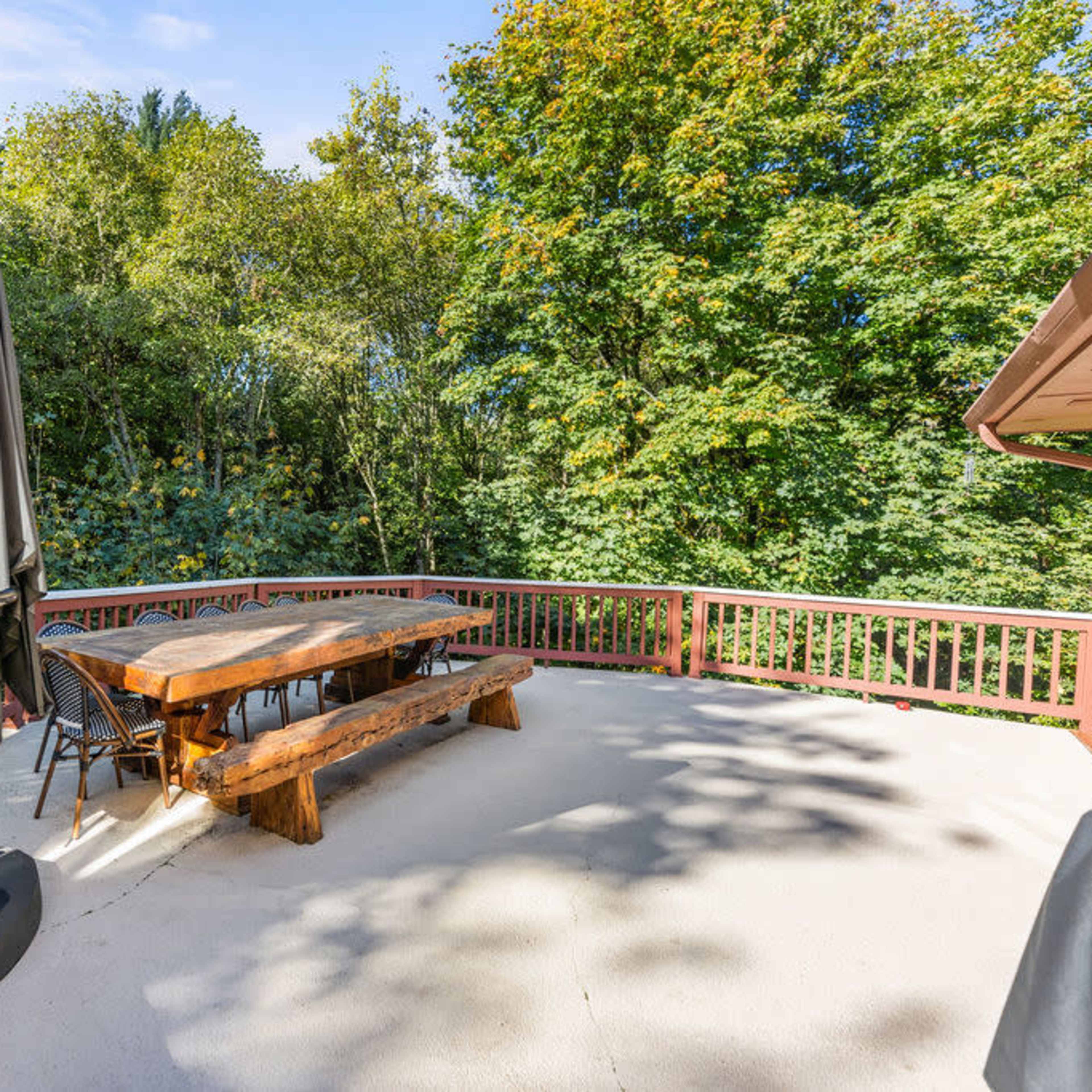 A wooden table with chairs is set on a patio surrounded by trees.
