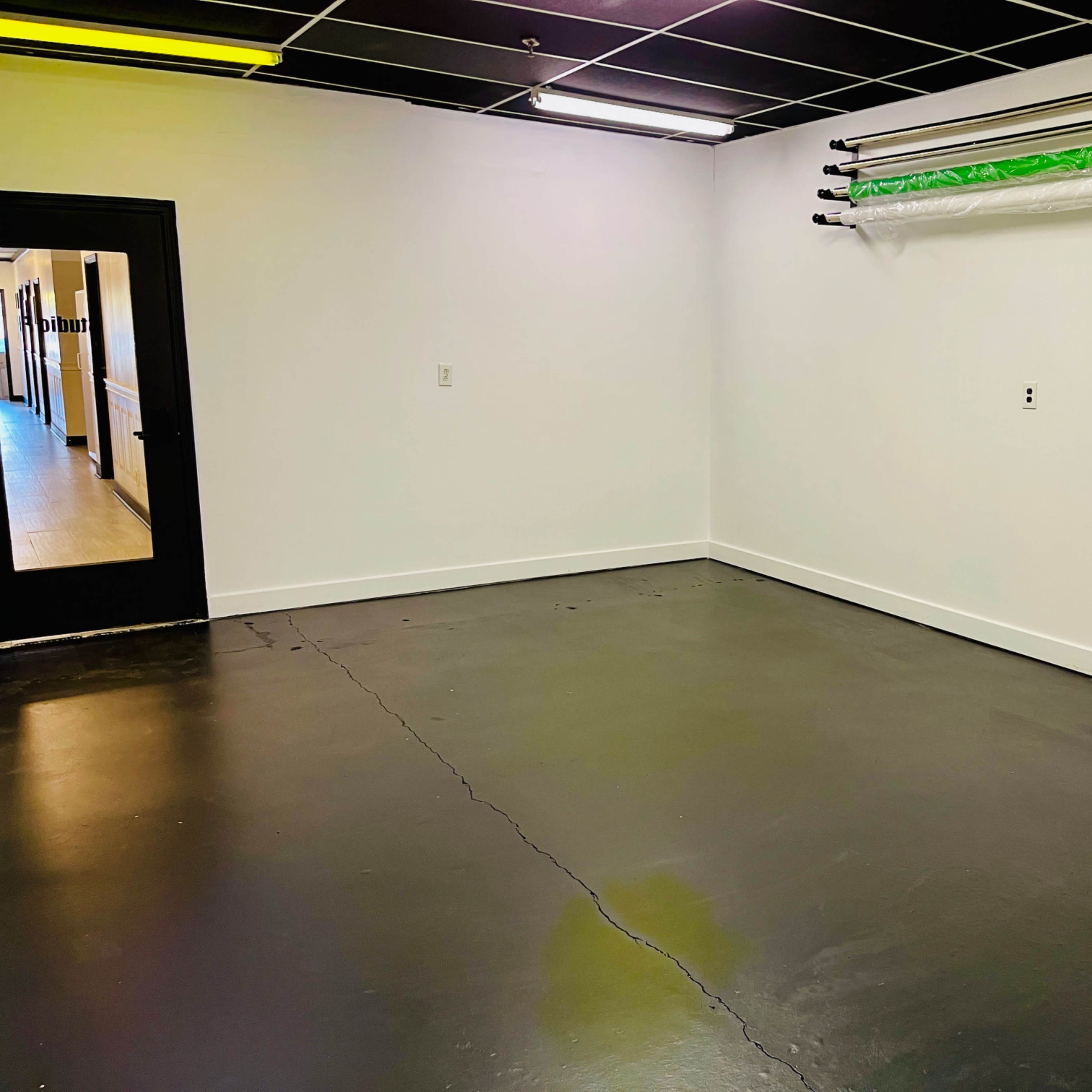 An empty room with a concrete floor, white walls, and a door leading to another space.