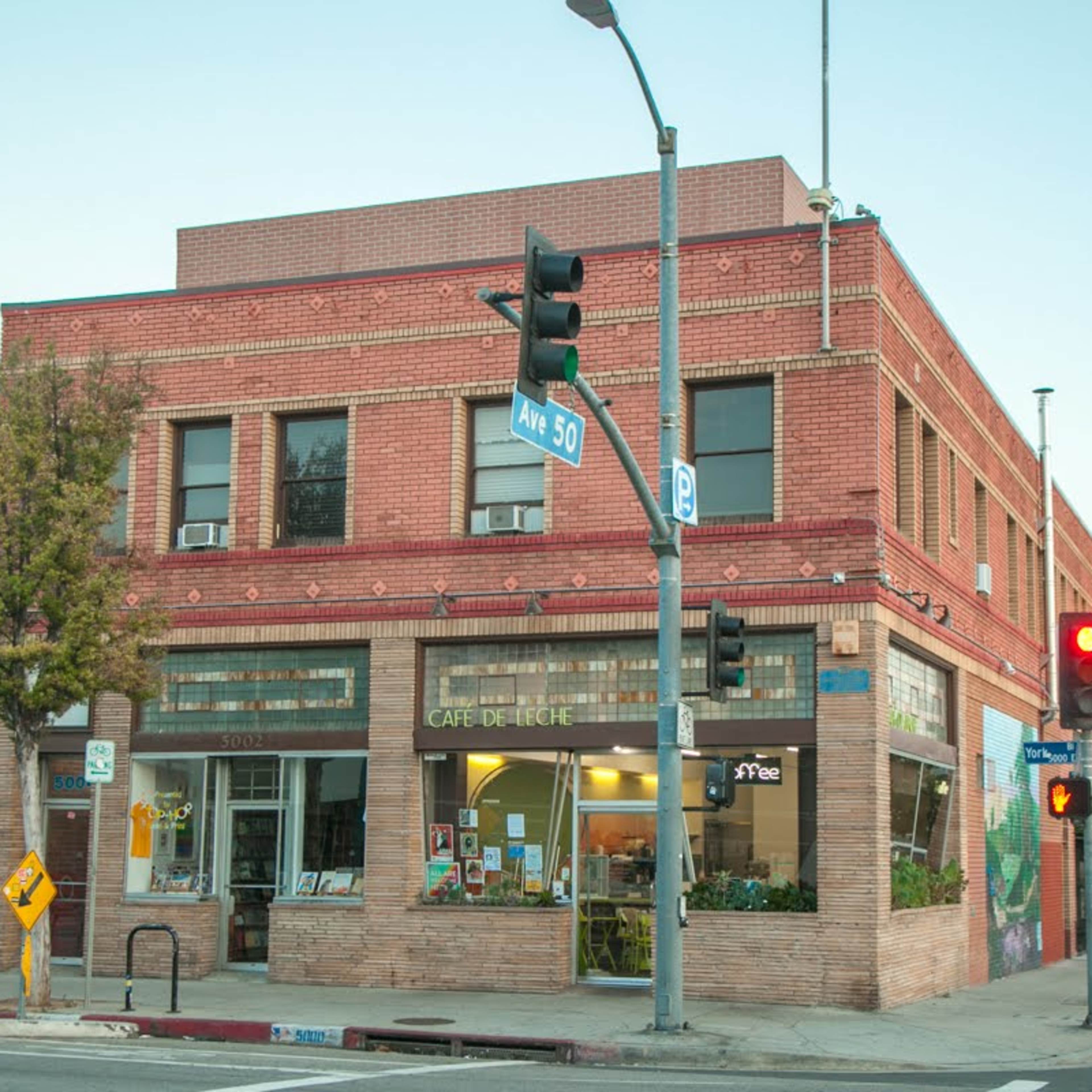 A brick building featuring a café called "Café de Linge" at a street corner with traffic lights and nearby trees.
