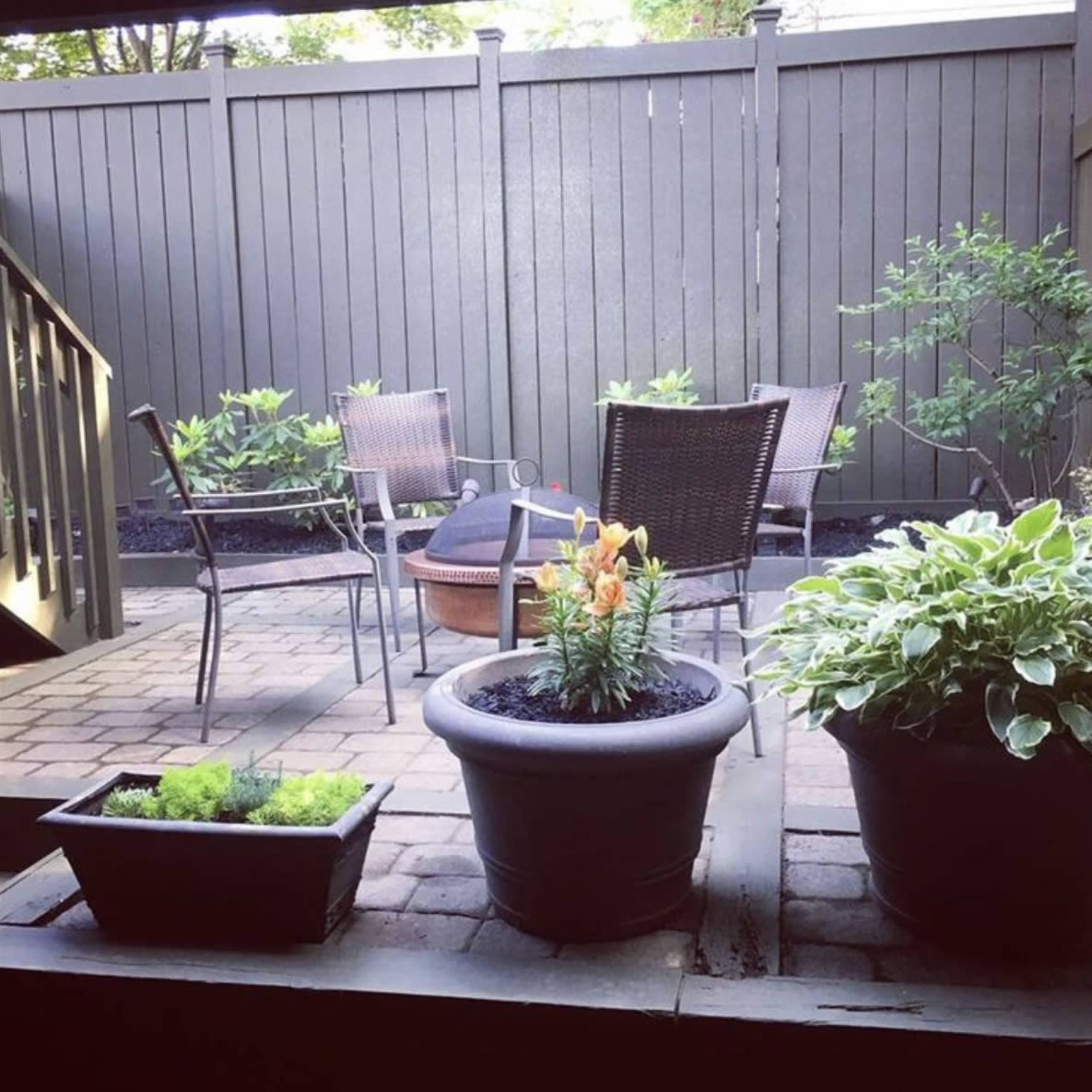 A patio area features potted plants, a fire pit, and four chairs arranged around a small table.