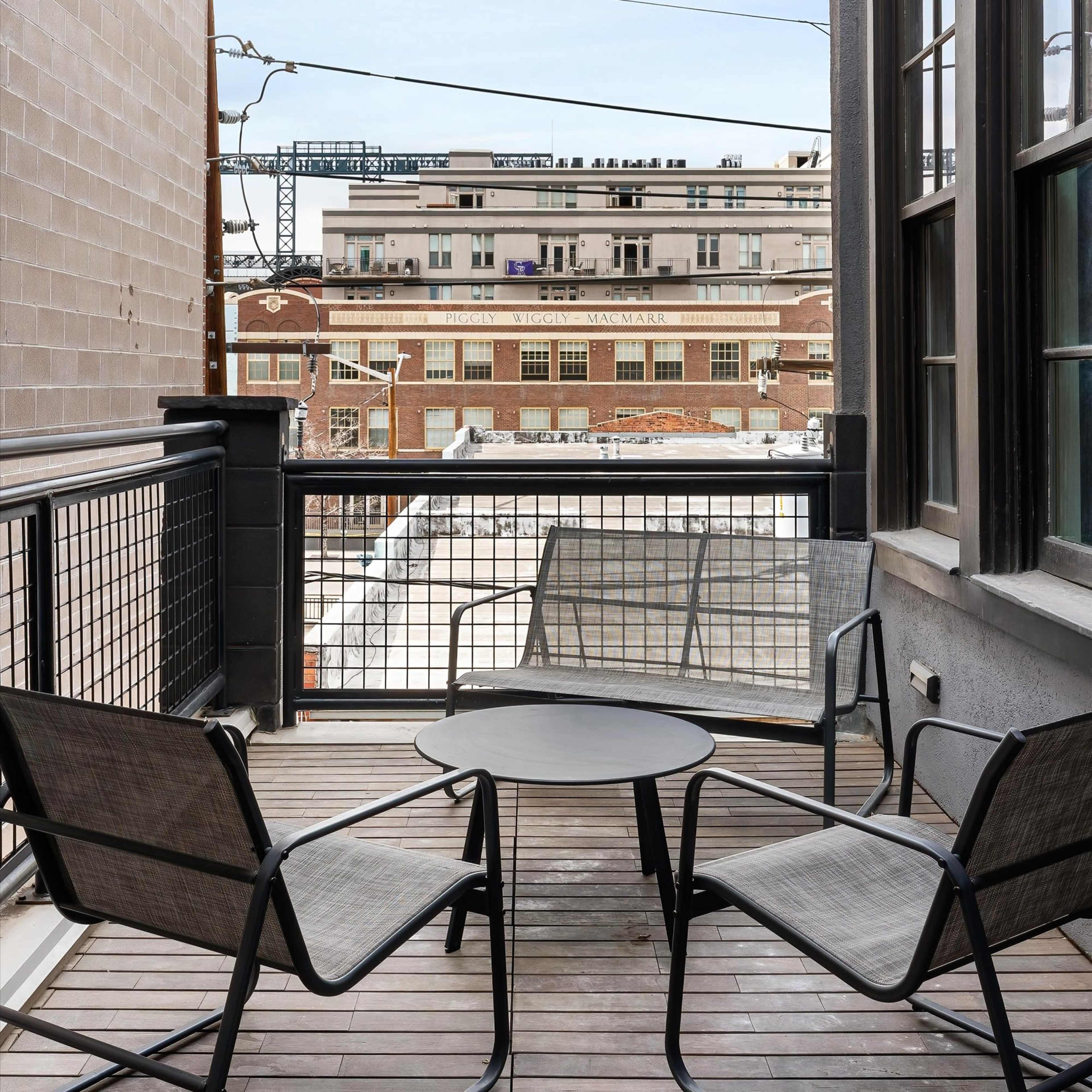 A small balcony with two chairs and a table, overlooking a view of buildings and power lines.